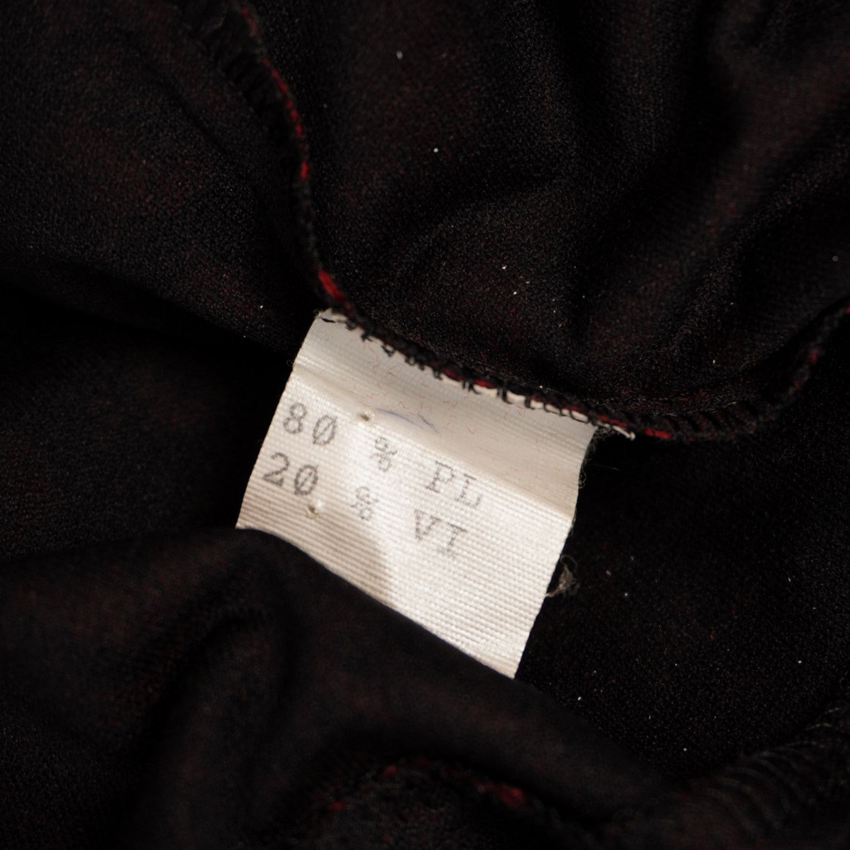 Dettaglio dell'etichetta tecnica interna che indica la composizione 80% poliestere e 20% viscosa della blusa.