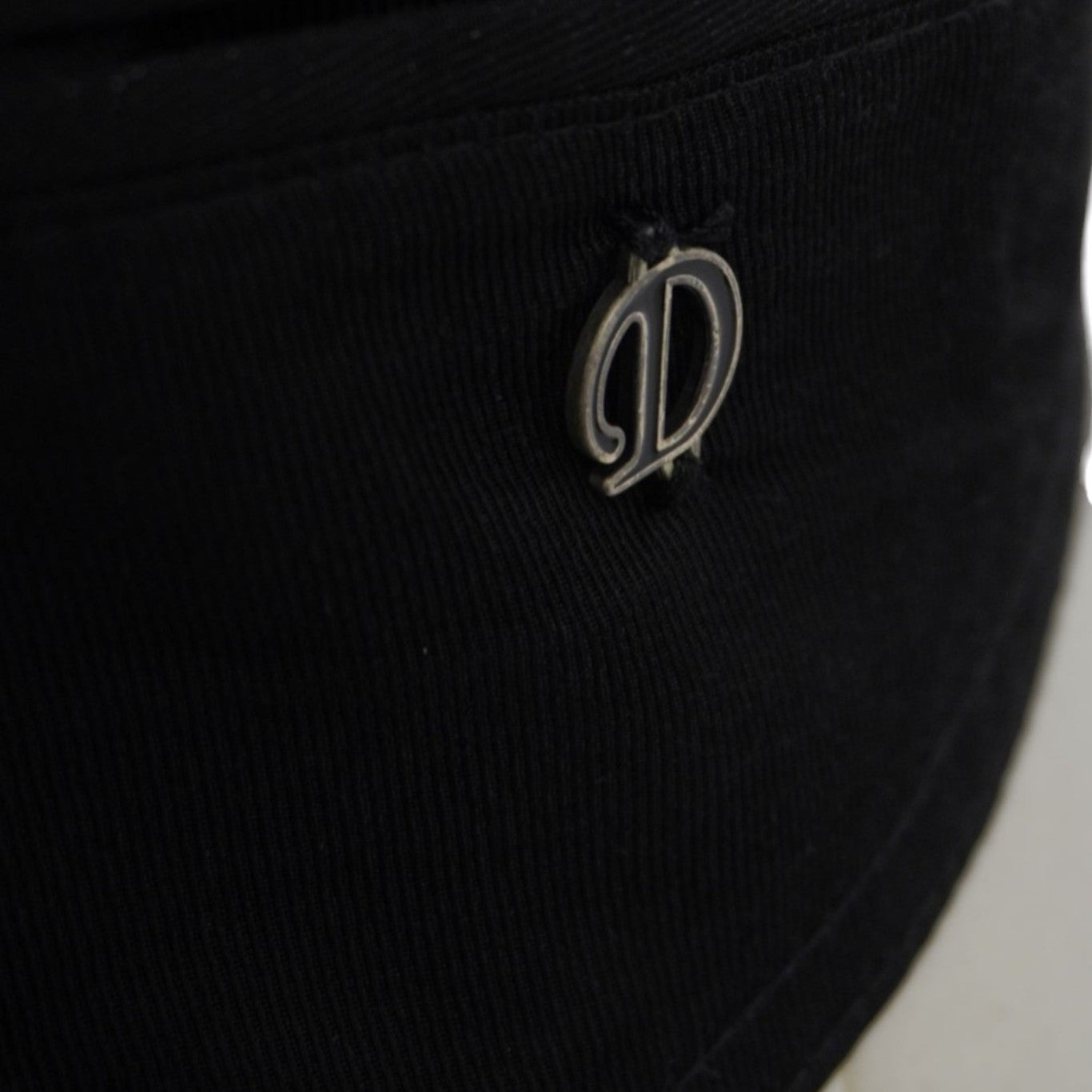 Primo piano del logo metallico Diesel "D" applicato lateralmente sul gilet vintage nero.