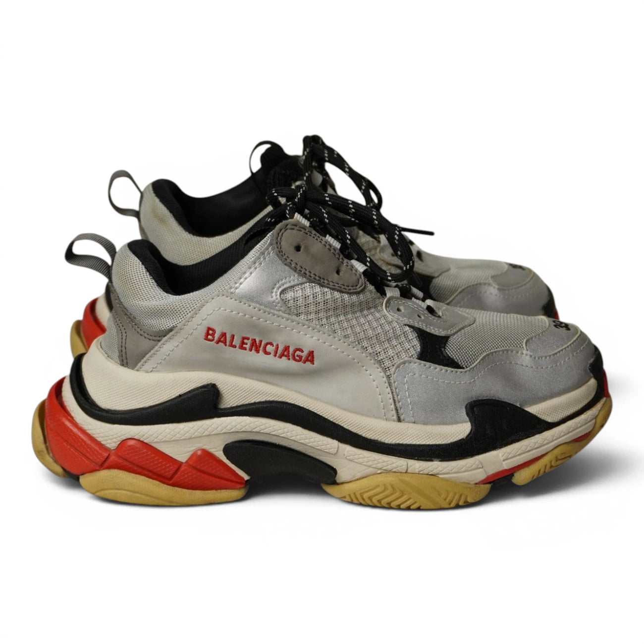 Sneakers Balenciaga Triple S grigie e argento usate viste di profilo con intersuola rossa.