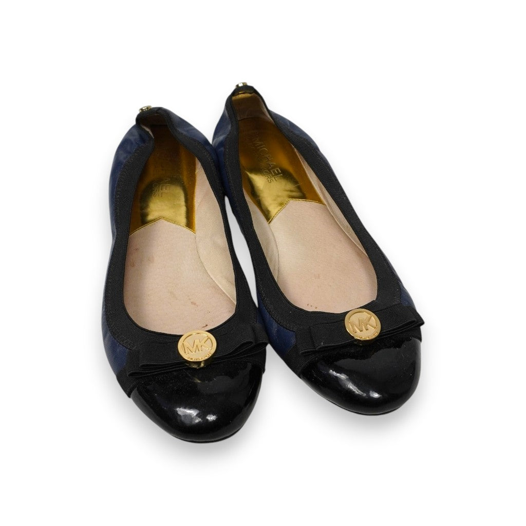 Vista frontale obliqua di un paio di ballerine Michael Michael Kors Dixie in pelle blu navy e punta cap-toe in vernice nera su sfondo bianco.