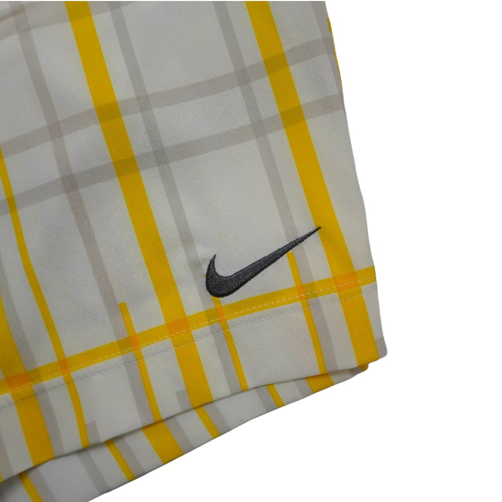 Inquadratura ravvicinata dell'iconico logo Swoosh Nike ricamato in filo nero sulla trama a scacchi gialla