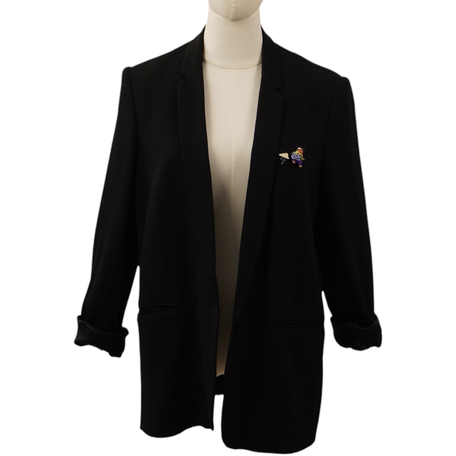 Vista frontale di un blazer nero monopetto Stella McCartney su un manichino, con revers classici e un'applicazione colorata sul taschino frontale.