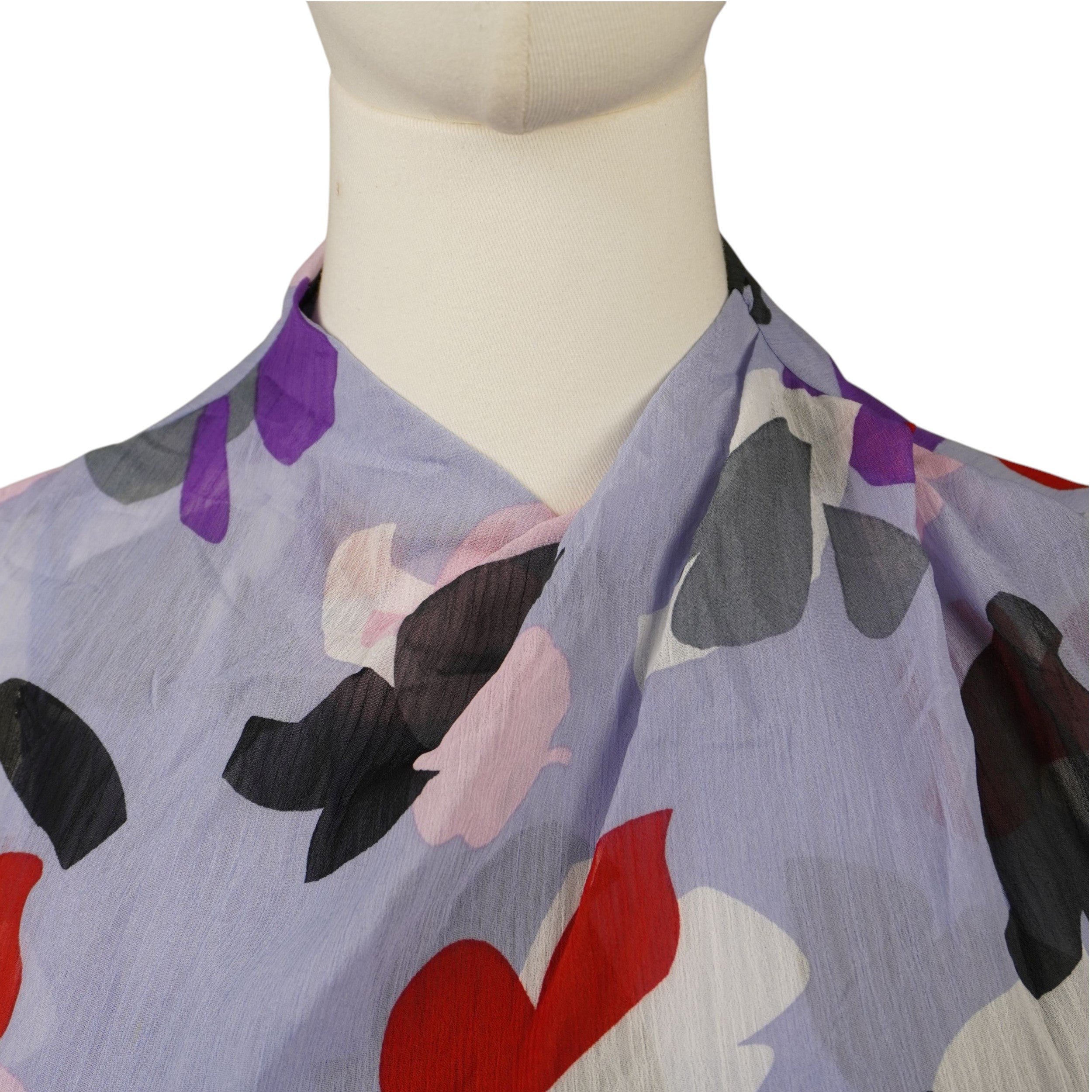 Dettaglio ravvicinato dello scollo incrociato e drappeggiato sul petto della blusa trasparente in chiffon lilla firmata Emporio Armani.