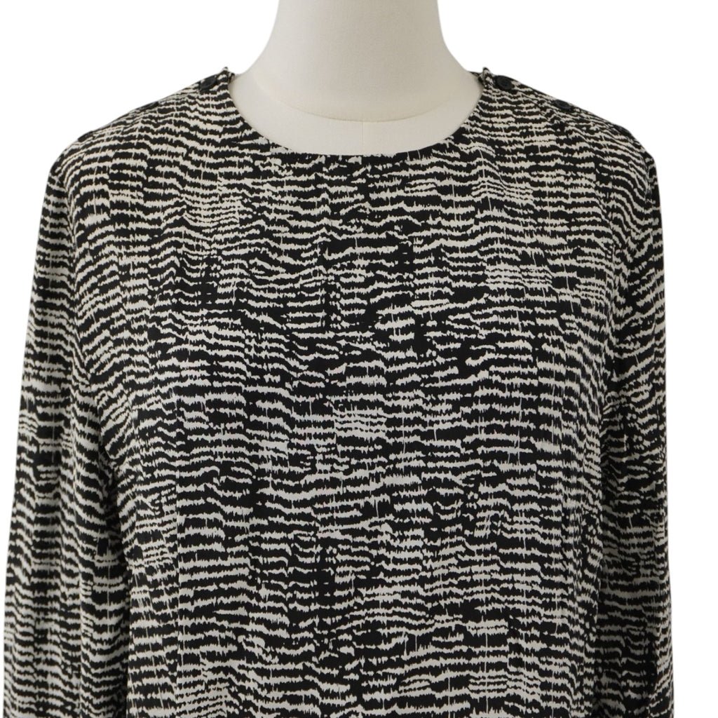  Inquadratura ravvicinata dello scollo a girocollo e del pattern grafico geometrico bianco e nero sulla parte superiore della blusa.
