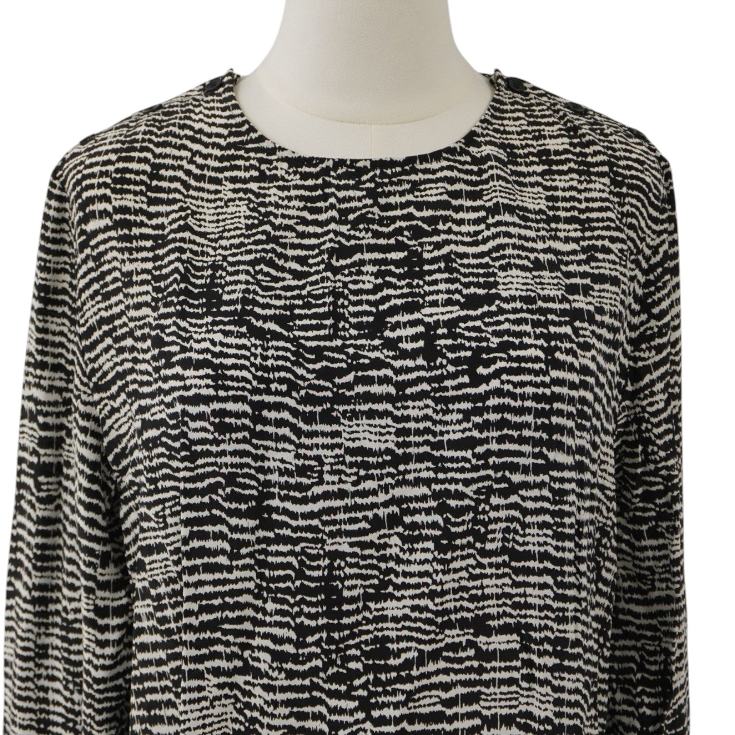  Inquadratura ravvicinata dello scollo a girocollo e del pattern grafico geometrico bianco e nero sulla parte superiore della blusa.