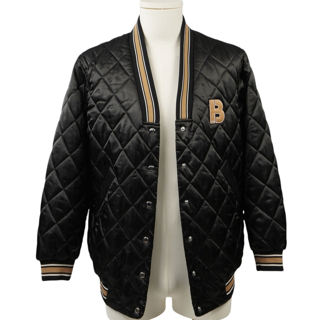 Vista frontale di un bomber nero satinato BOSS modello Jesata trapuntato a diamante su manichino, con maxi patch monogramma B dorata sul petto e bordi in maglia a coste.