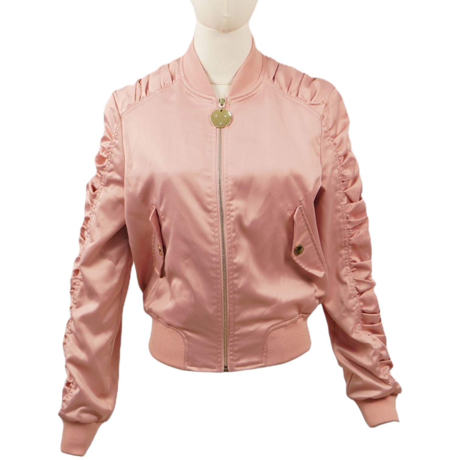 Vista frontale del bomber satinato rosa cipria Guess Selvaggia su un manichino, con maniche arricciate, chiusura zip e tiralampo tondo dorato.