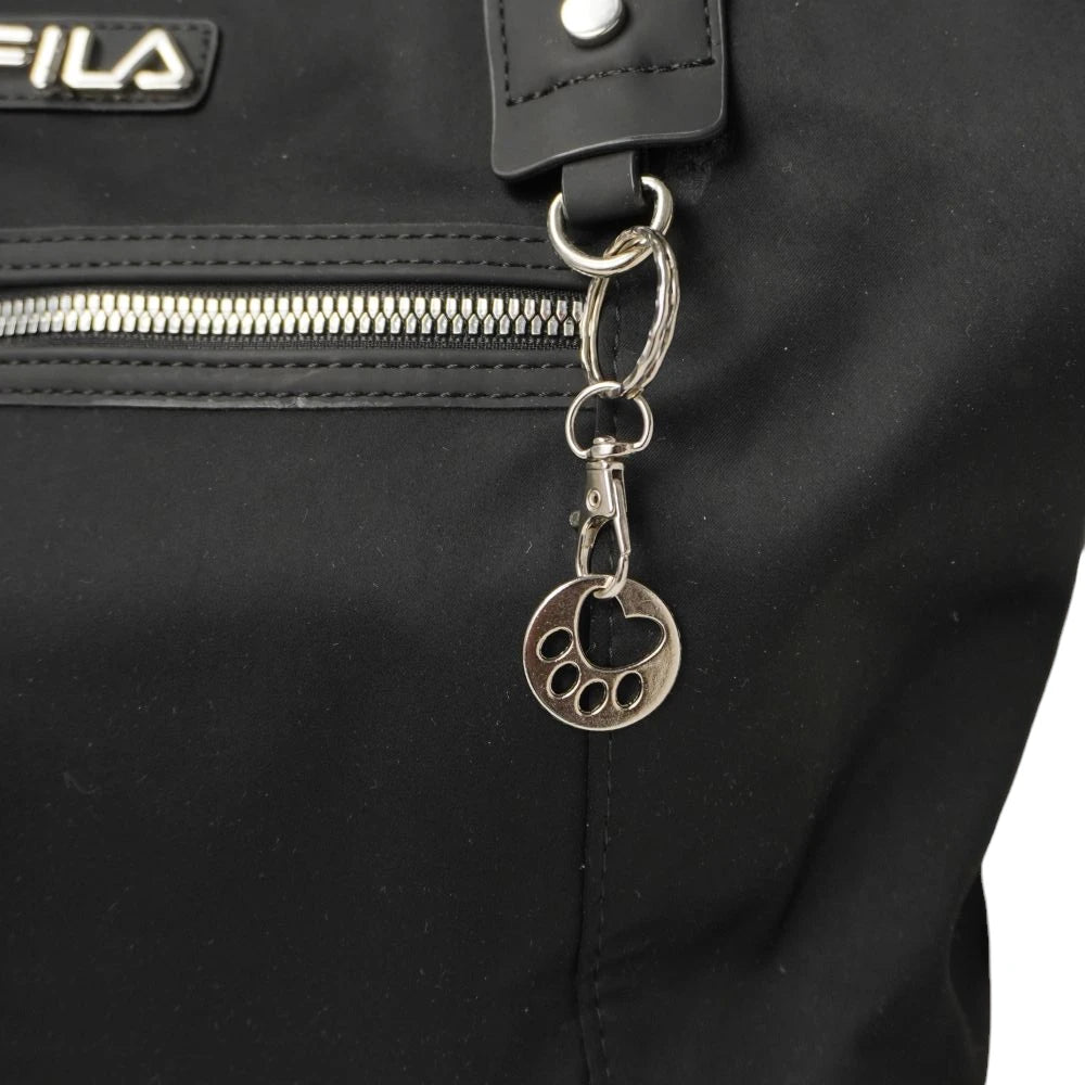 Primo piano del ciondolo charm in metallo argentato a forma di zampina di animale con cuore centrale, agganciato alla borsa FILA.
