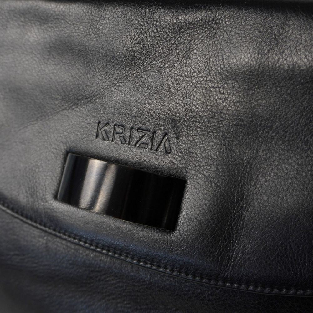 Primo piano del logo Krizia impresso a caldo sulla pelle nera sopra la maxi chiusura geometrica centrale in resina nera lucida.