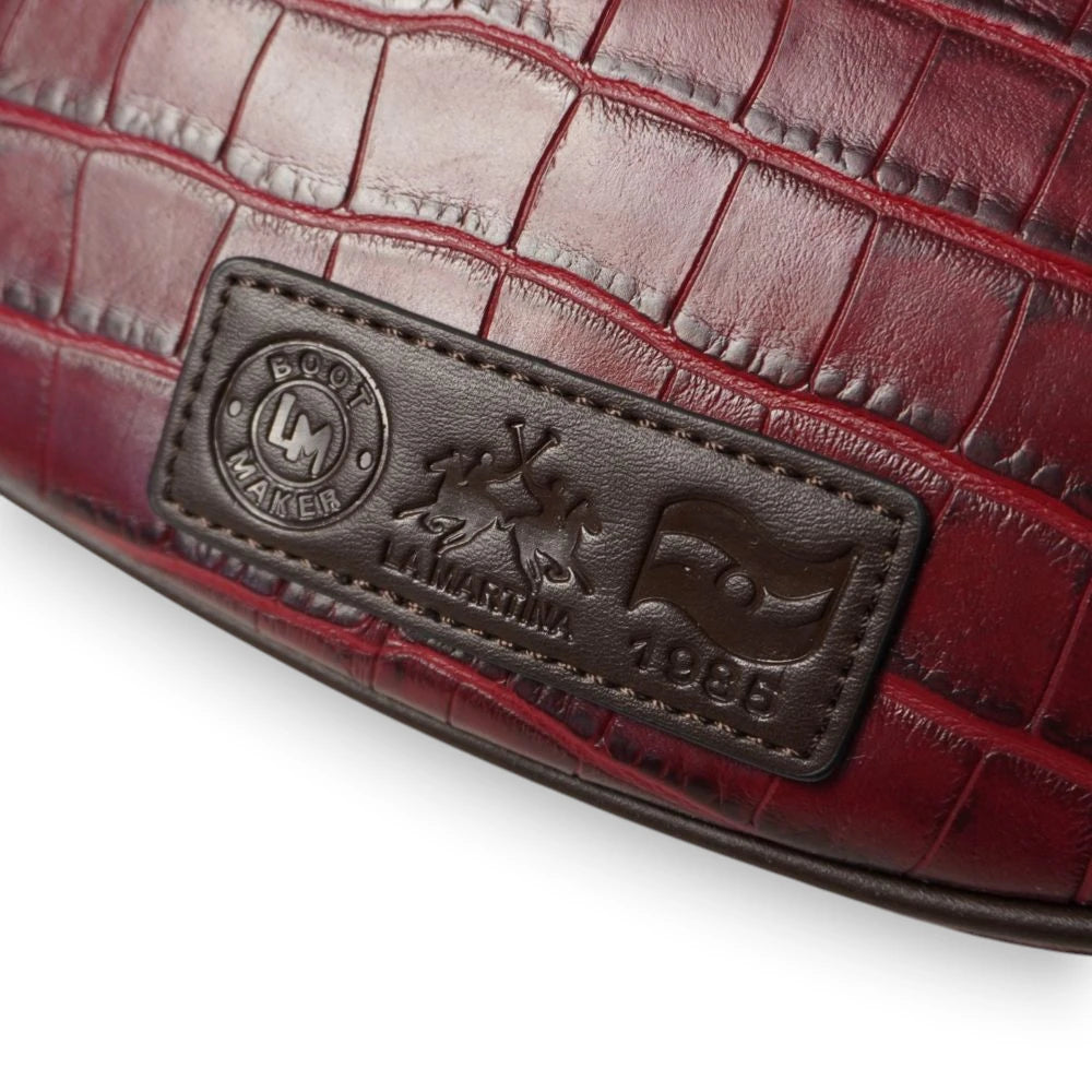 Primo piano del patch rettangolare in pelle marrone scuro cucito sul retro della borsa La Martina con impressi i loghi Boot Maker e l'anno 1985.