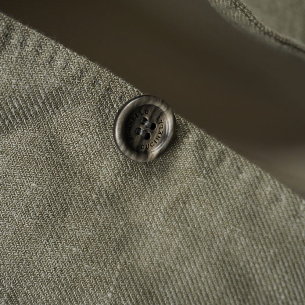 Particolare del bottone in corno naturale con incisione del marchio Brunello Cucinelli su tessuto fiammato verde.