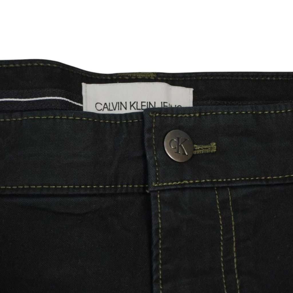 Dettaglio del bottone metallico inciso CK e dell'etichetta bianca interna dei pantaloni Calvin Klein Jeans