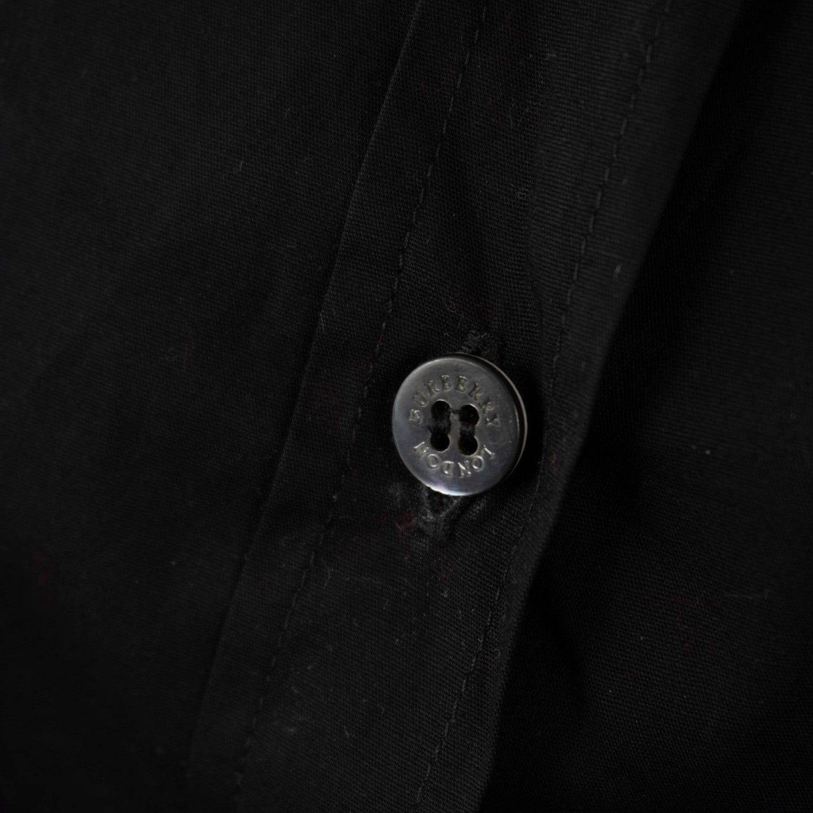 Close-up di un bottone nero cucito sul tessuto scuro con inciso il logo ufficiale del brand Burberry London.