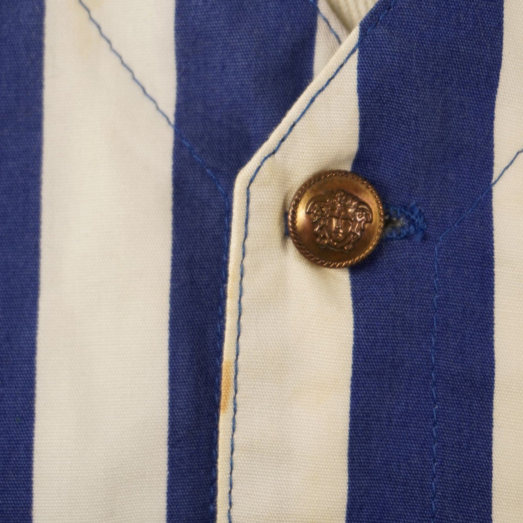 Dettaglio del bottone dorato originale con testa di Medusa e leggera macchia sul gilet Versace Jeans Couture