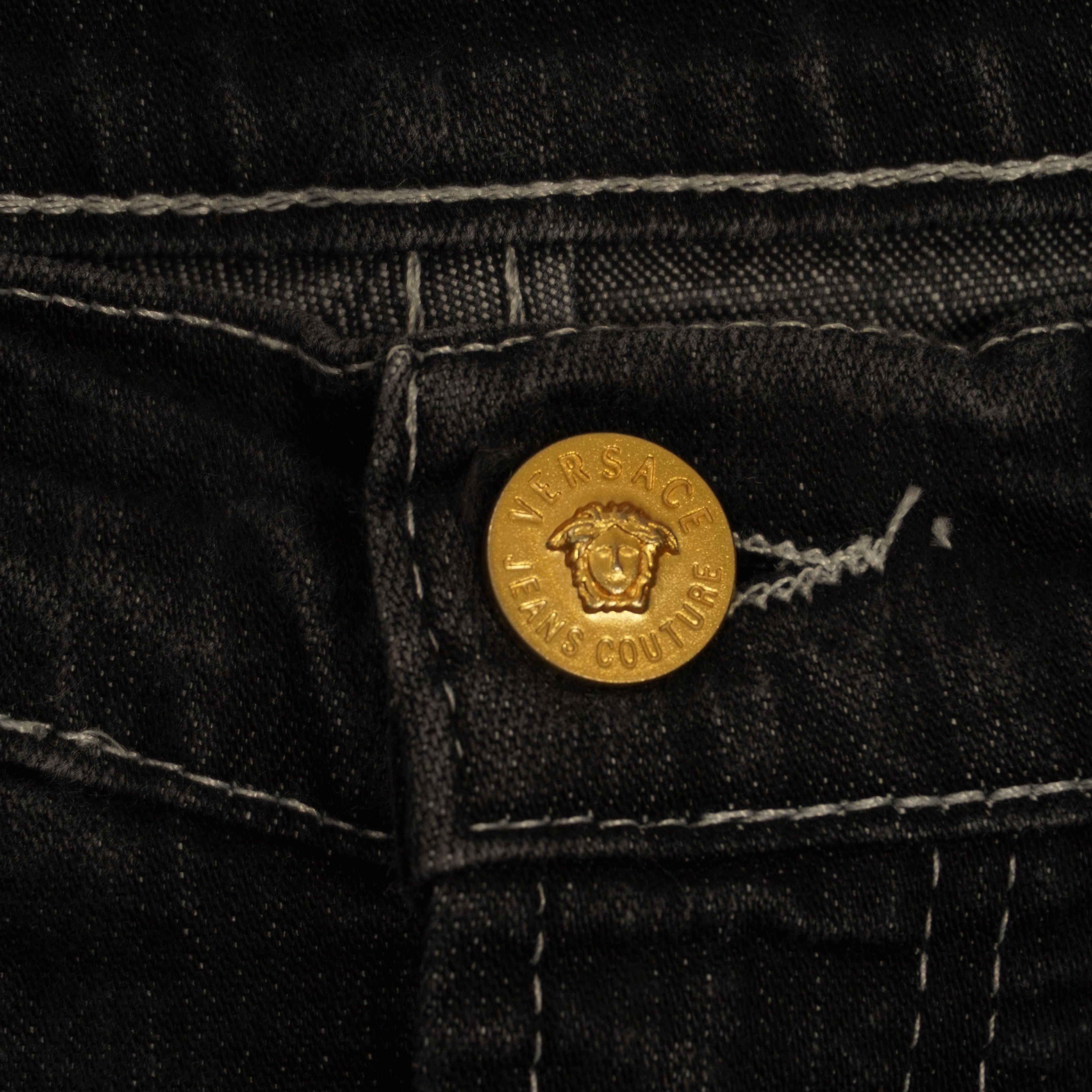 Dettaglio macro del bottone frontale in metallo dorato inciso con l'iconico logo della testa di Medusa Versace.