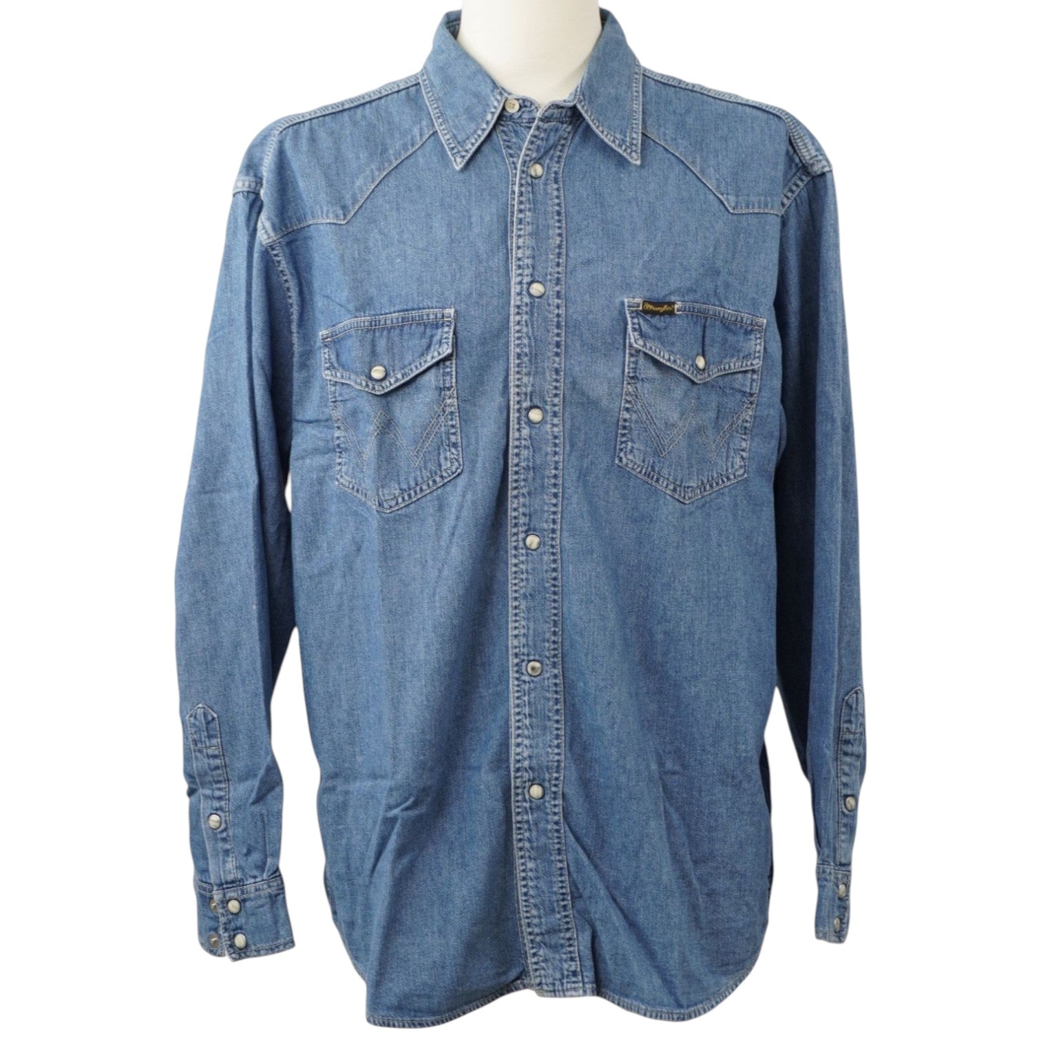Vista frontale su manichino di una camicia di jeans azzurra Wrangler Authentic Western a maniche lunghe, con tasche sul petto e bottoni automatici.
