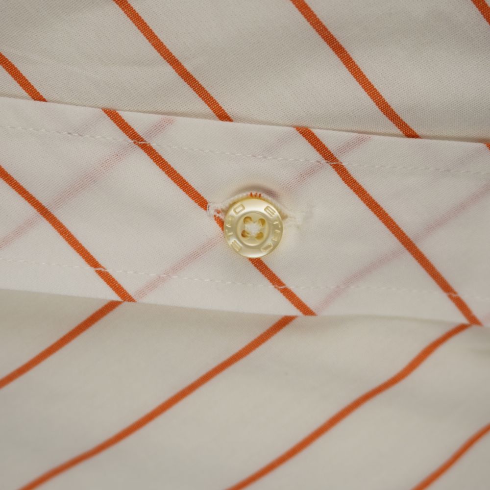 Dettaglio macro di un bottone chiaro della camicia con la scritta ETRO incisa a sbalzo lungo il bordo circolare.