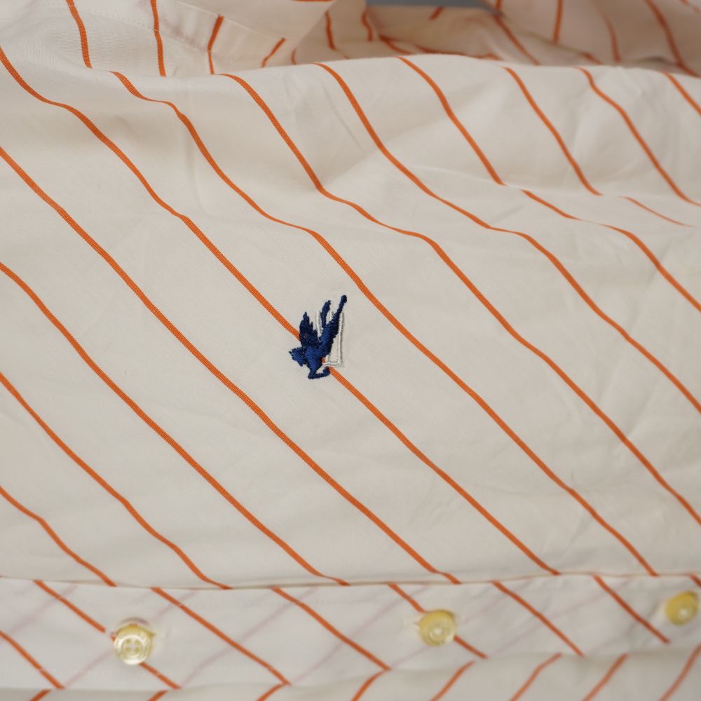Primo piano ravvicinato del mitologico cavallo alato Pegaso di Etro ricamato in filo blu navy sopra la trama a righe arancioni.