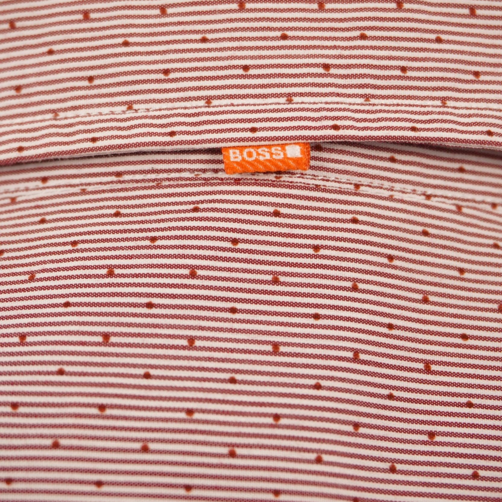 Dettaglio della micro-trama del tessuto dobby rosso Hugo Boss con focus sulla piccola asola e sulla fettuccia arancione sul retro.