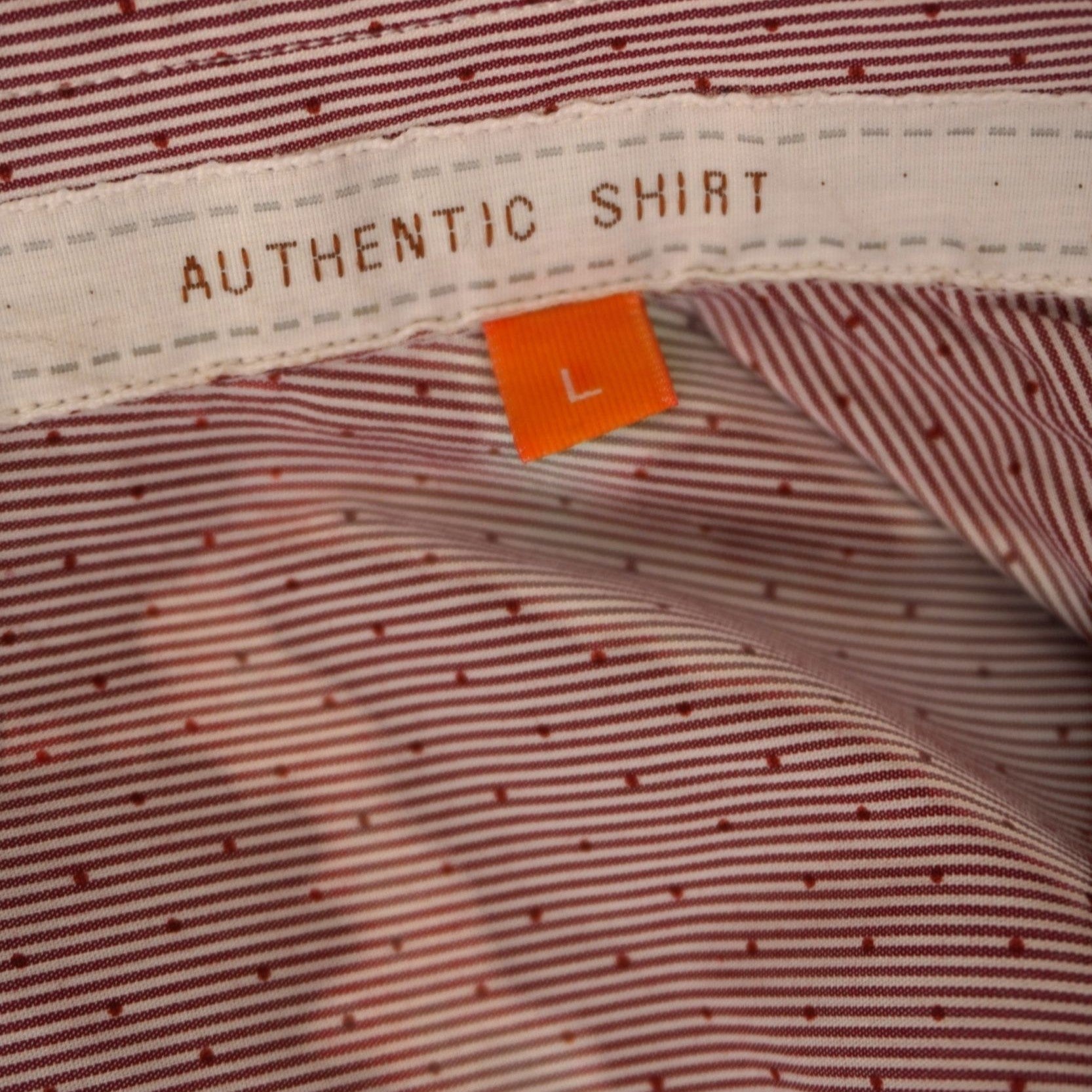 Primo piano del nastro interno al colletto con la scritta ricamata Authentic Shirt posizionato sopra l'etichetta arancione Hugo Boss.