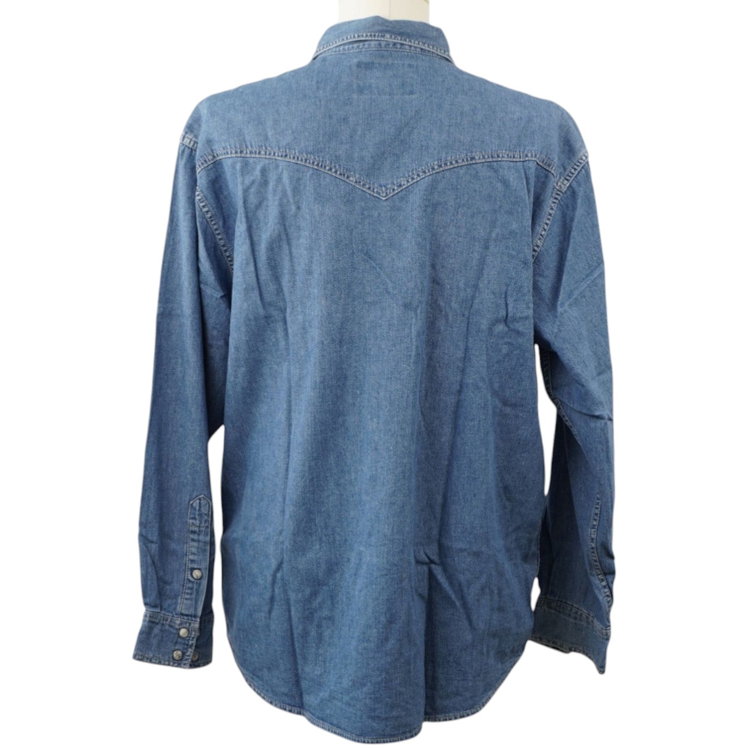 Inquadratura posteriore intera su manichino della camicia denim Wrangler, che evidenzia il taglio dritto e il carrè a punta stile western sulle spalle.