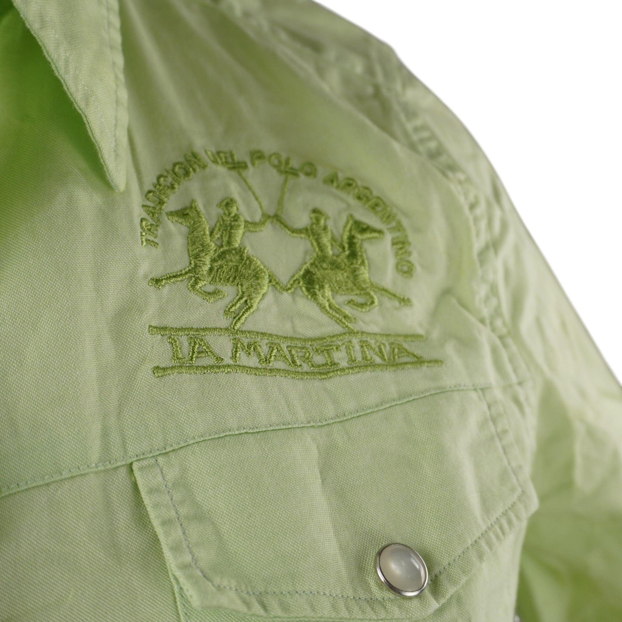 Primo piano del logo La Martina Tradicion del Polo Argentino ricamato in filo verde tono su tono sopra la patta del taschino sul petto.