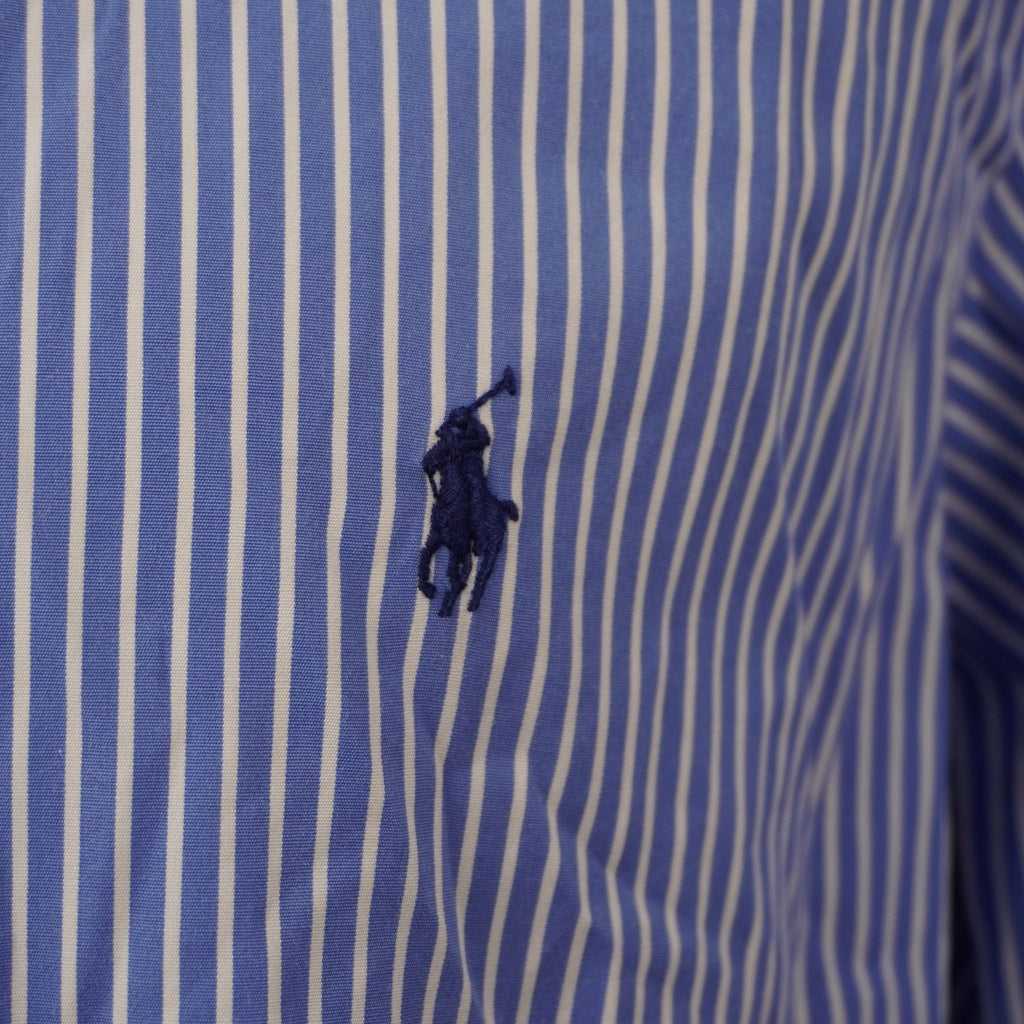 Inquadratura ravvicinata dell'iconico logo del pony Ralph Lauren ricamato in filo blu scuro a contrasto sul tessuto a righe azzurre.