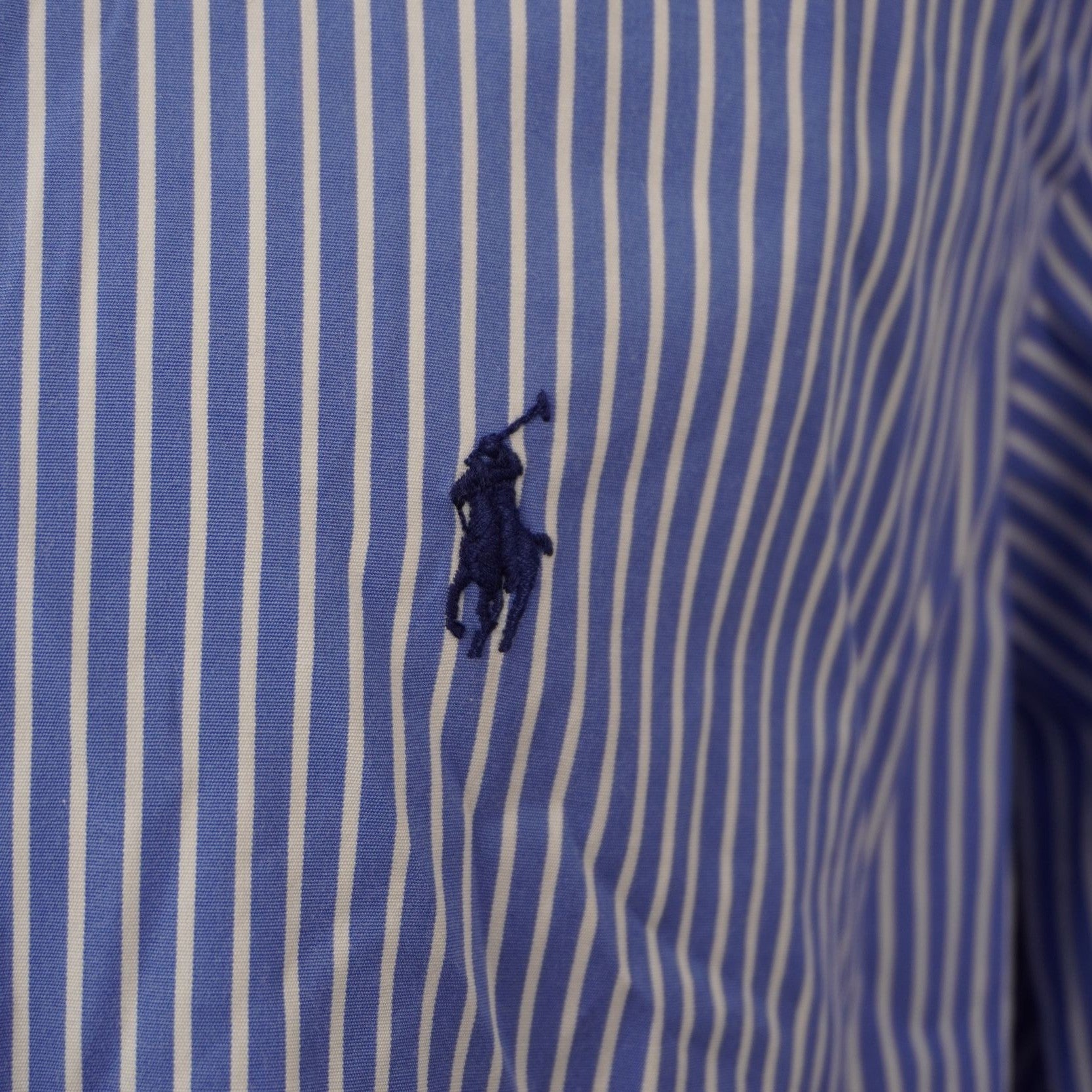 Inquadratura ravvicinata dell'iconico logo del pony Ralph Lauren ricamato in filo blu scuro a contrasto sul tessuto a righe azzurre.