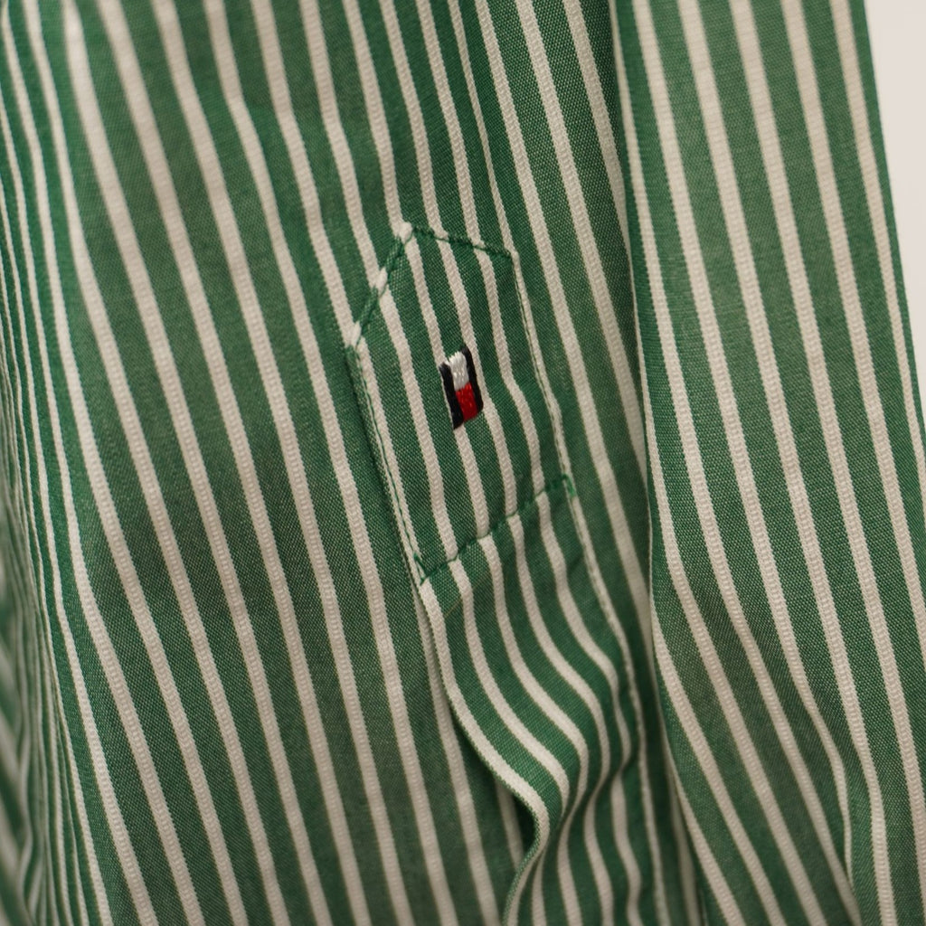 Inquadratura ravvicinata del polsino con bottone e dello spacco della manica lunga della camicia a righe verdi.