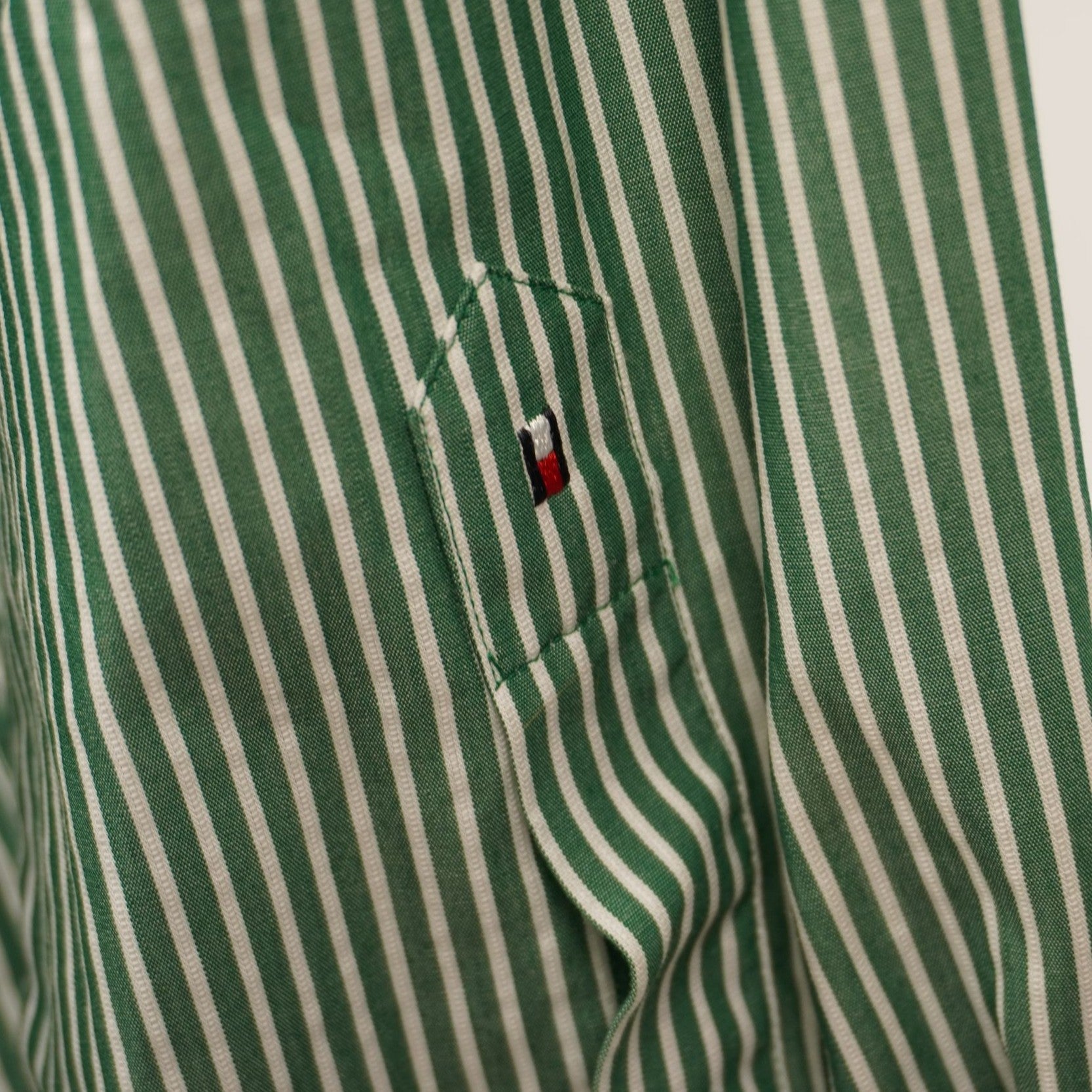 Inquadratura ravvicinata del polsino con bottone e dello spacco della manica lunga della camicia a righe verdi.