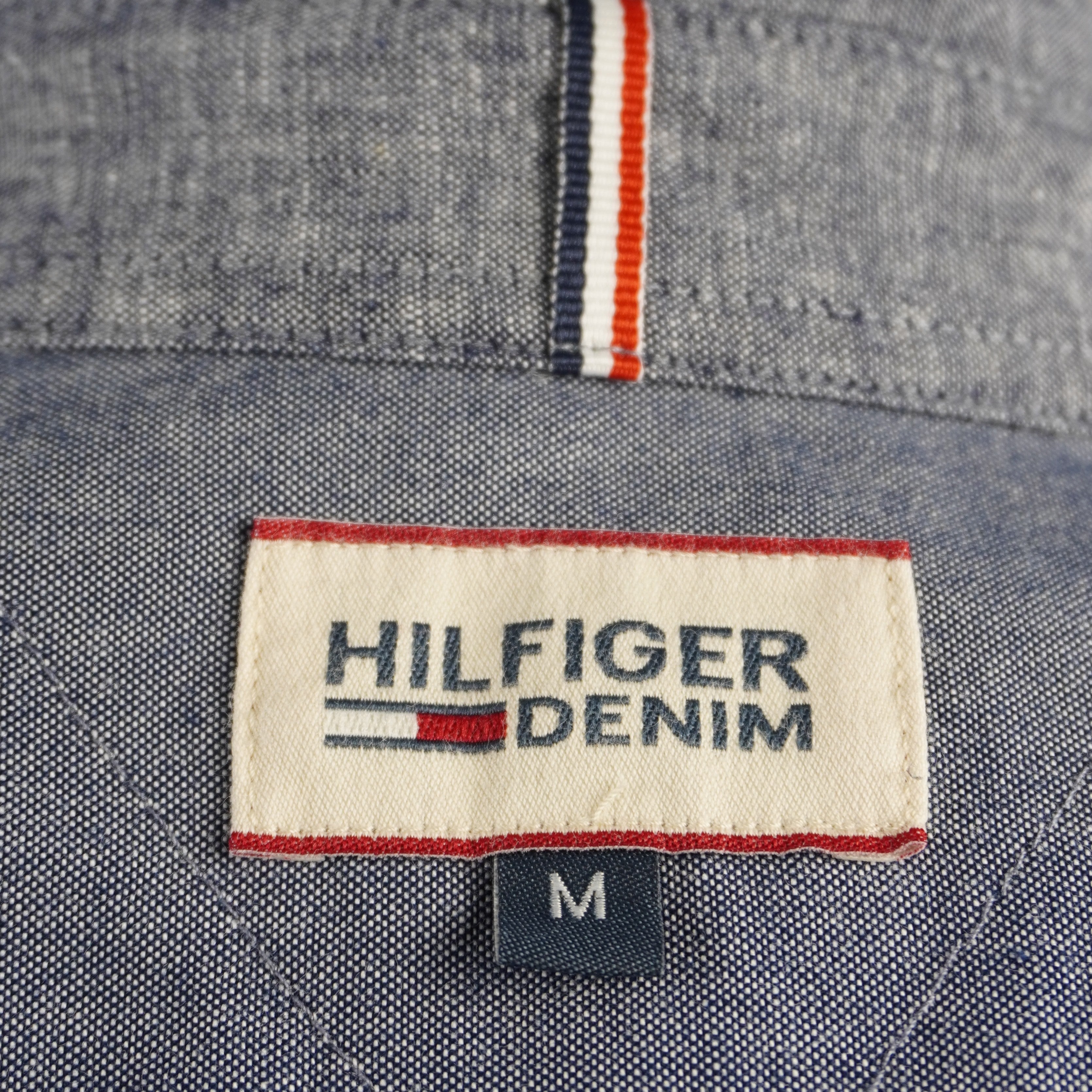 Etichetta interna Hilfiger Denim con nastro iconico tricolore (rosso, bianco, blu) nel sottocollo, dettaglio di autenticità premium.