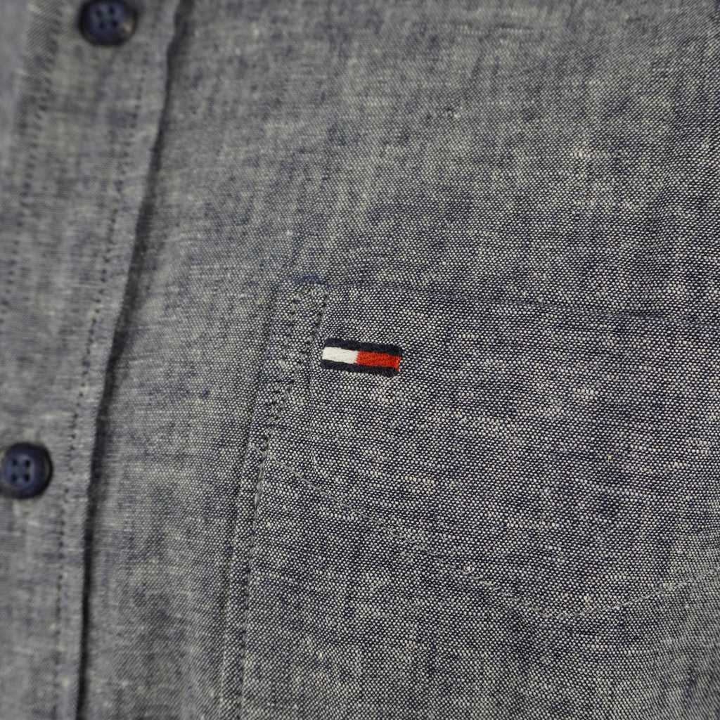 Primo piano del piccolo logo "flag" Tommy Hilfiger ricamato sul petto, dettaglio della trama del tessuto Oxford melange.