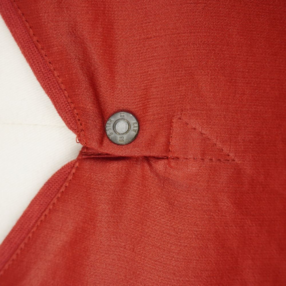 Primo piano ravvicinato dello scollo a V del top rosso G-Star Raw con il dettaglio del bottone metallico inciso.