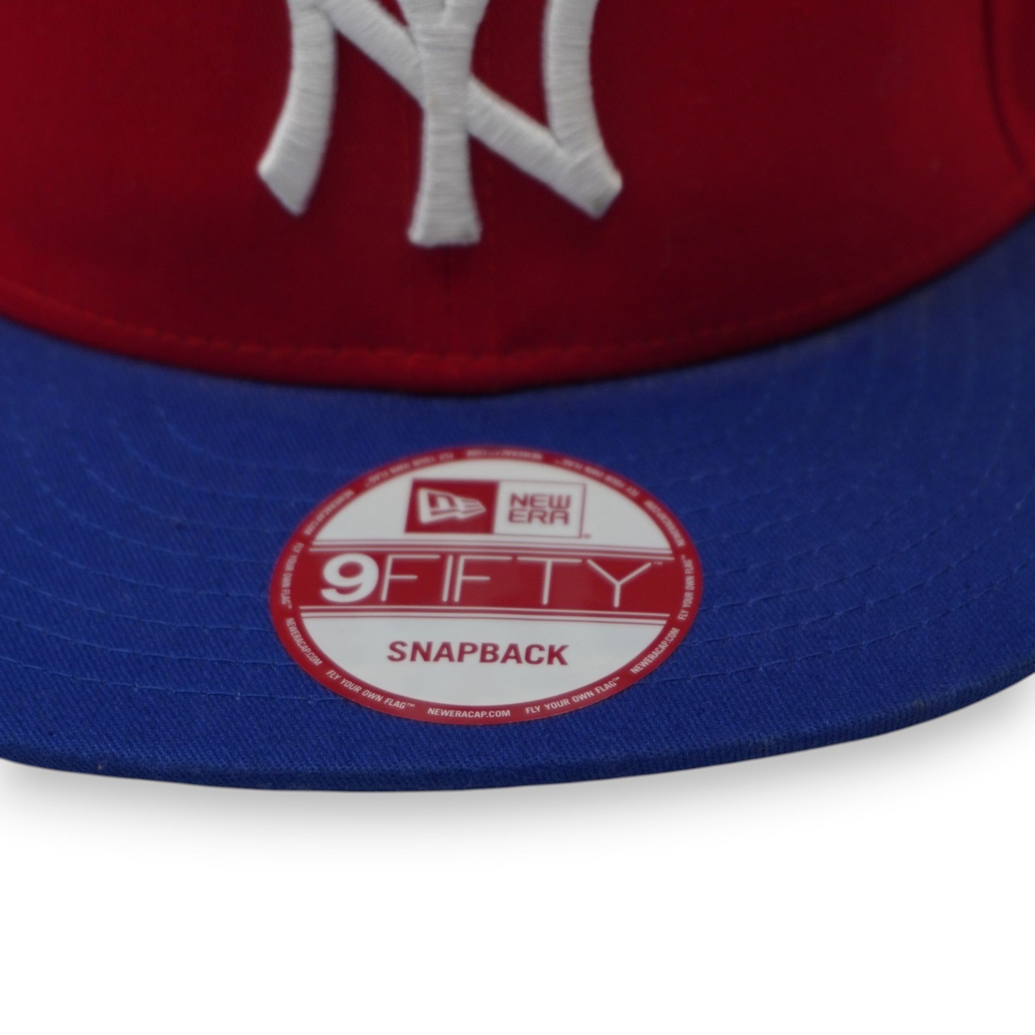 Primo piano della visiera piatta blu con lo sticker ufficiale olografico e circolare rosso e argento New Era 9FIFTY Snapback.