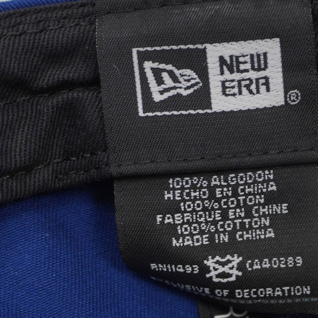 Dettaglio dell'etichetta interna di composizione New Era che certifica il tessuto in 100% cotone e riporta i codici RN e CA.