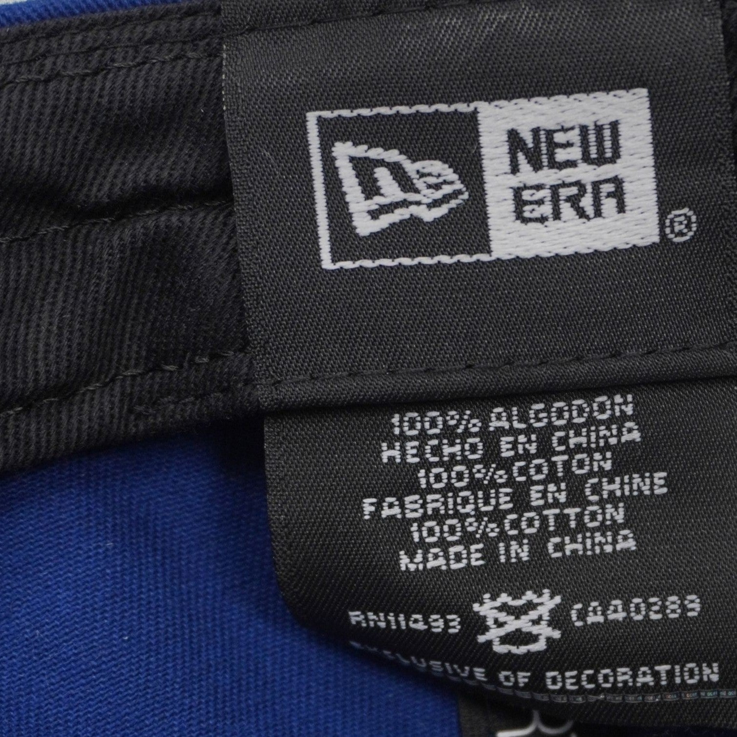 Dettaglio dell'etichetta interna di composizione New Era che certifica il tessuto in 100% cotone e riporta i codici RN e CA.