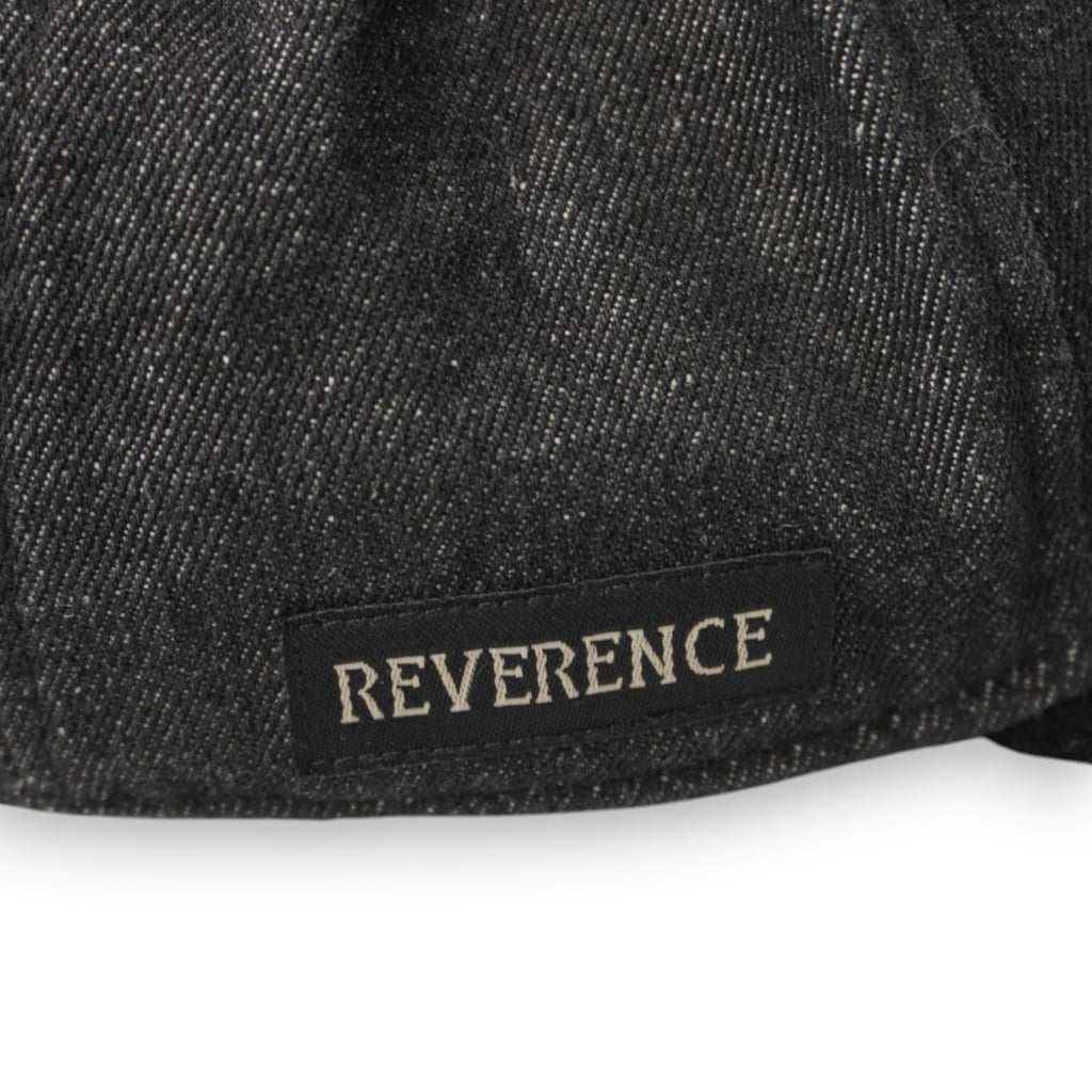 Zoom sulla patch rettangolare in tessuto nero con la scritta ricamata grigia REVERENCE posizionata sul lato destro del cappello.
