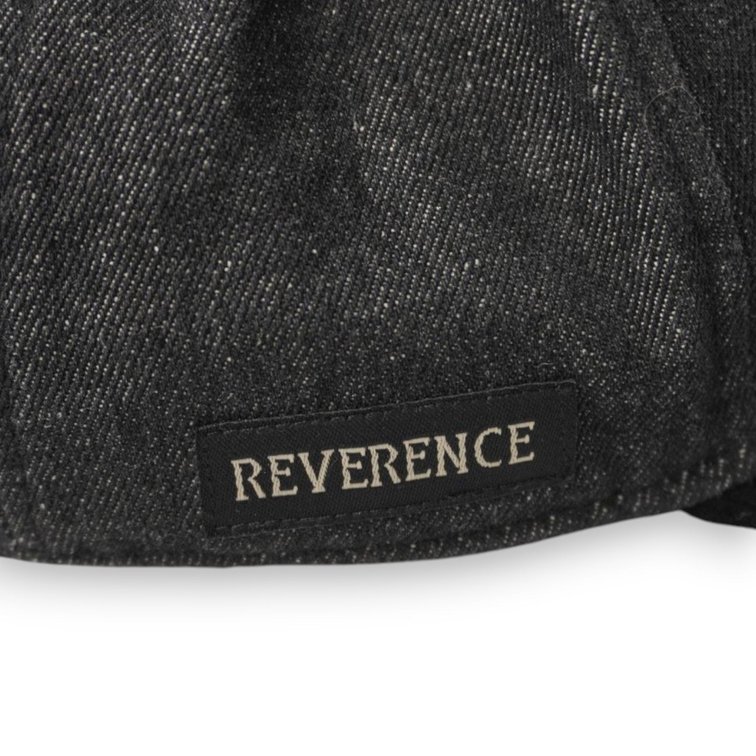 Zoom sulla patch rettangolare in tessuto nero con la scritta ricamata grigia REVERENCE posizionata sul lato destro del cappello.