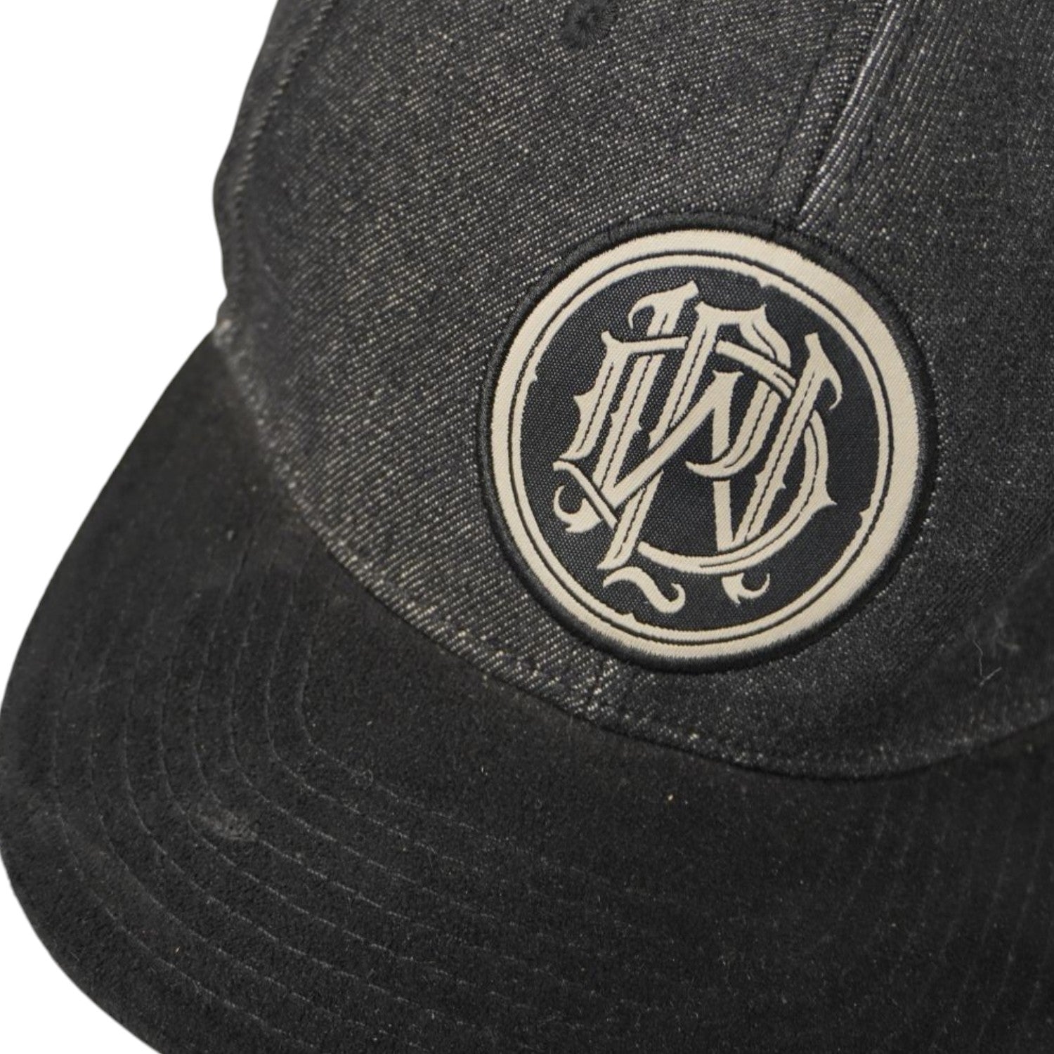 Dettaglio ravvicinato della toppa circolare frontale con il monogramma gotico PWD ricamato sul cappellino dei Parkway Drive.