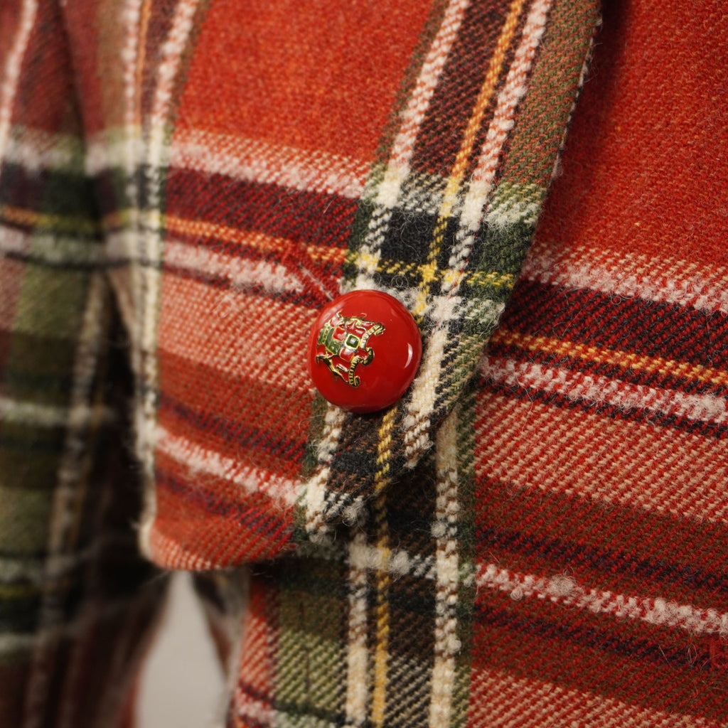 Inquadratura ravvicinata della tasca laterale a pattina con bottone rosso decorativo sul cappotto scozzese Les Copains.
