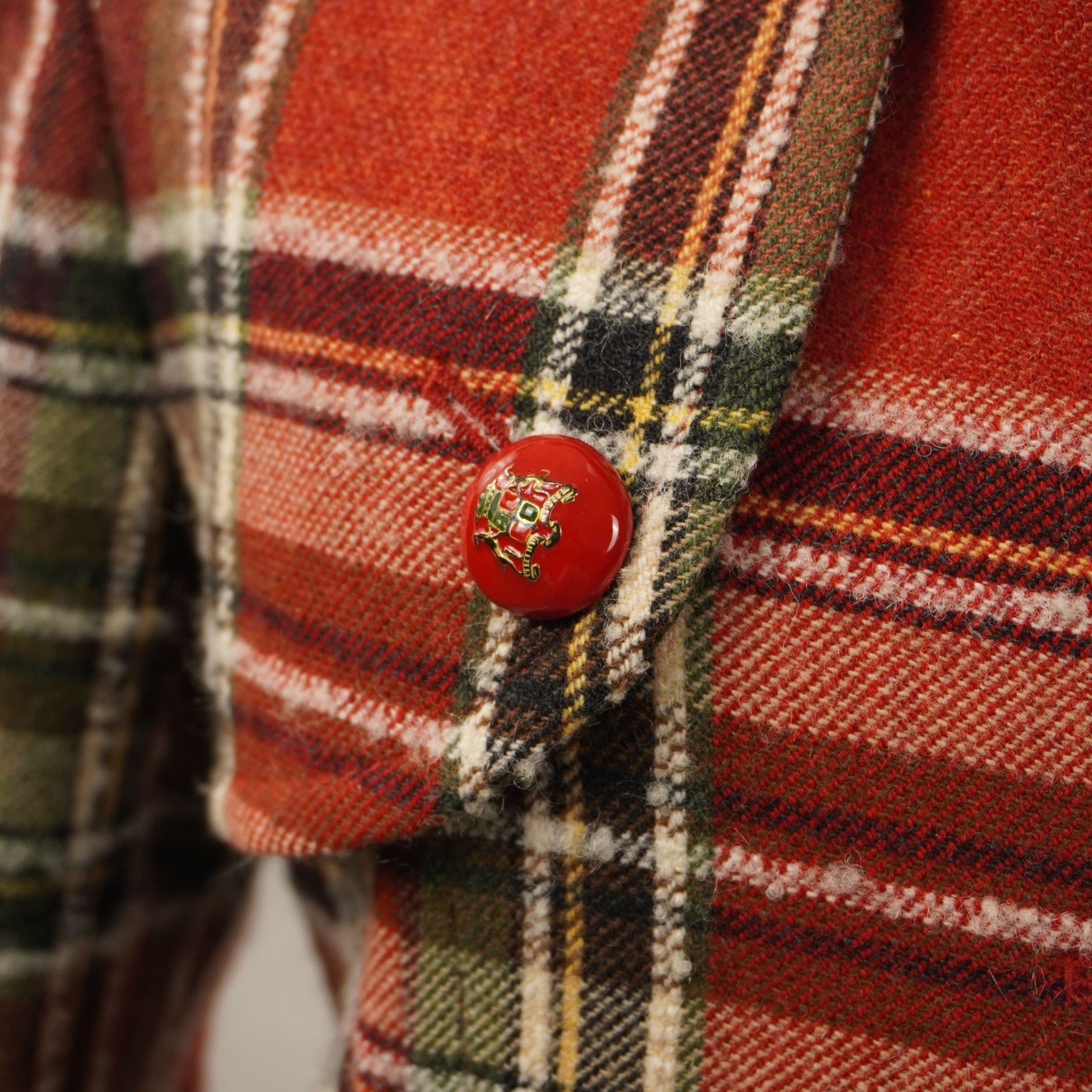 Inquadratura ravvicinata della tasca laterale a pattina con bottone rosso decorativo sul cappotto scozzese Les Copains.