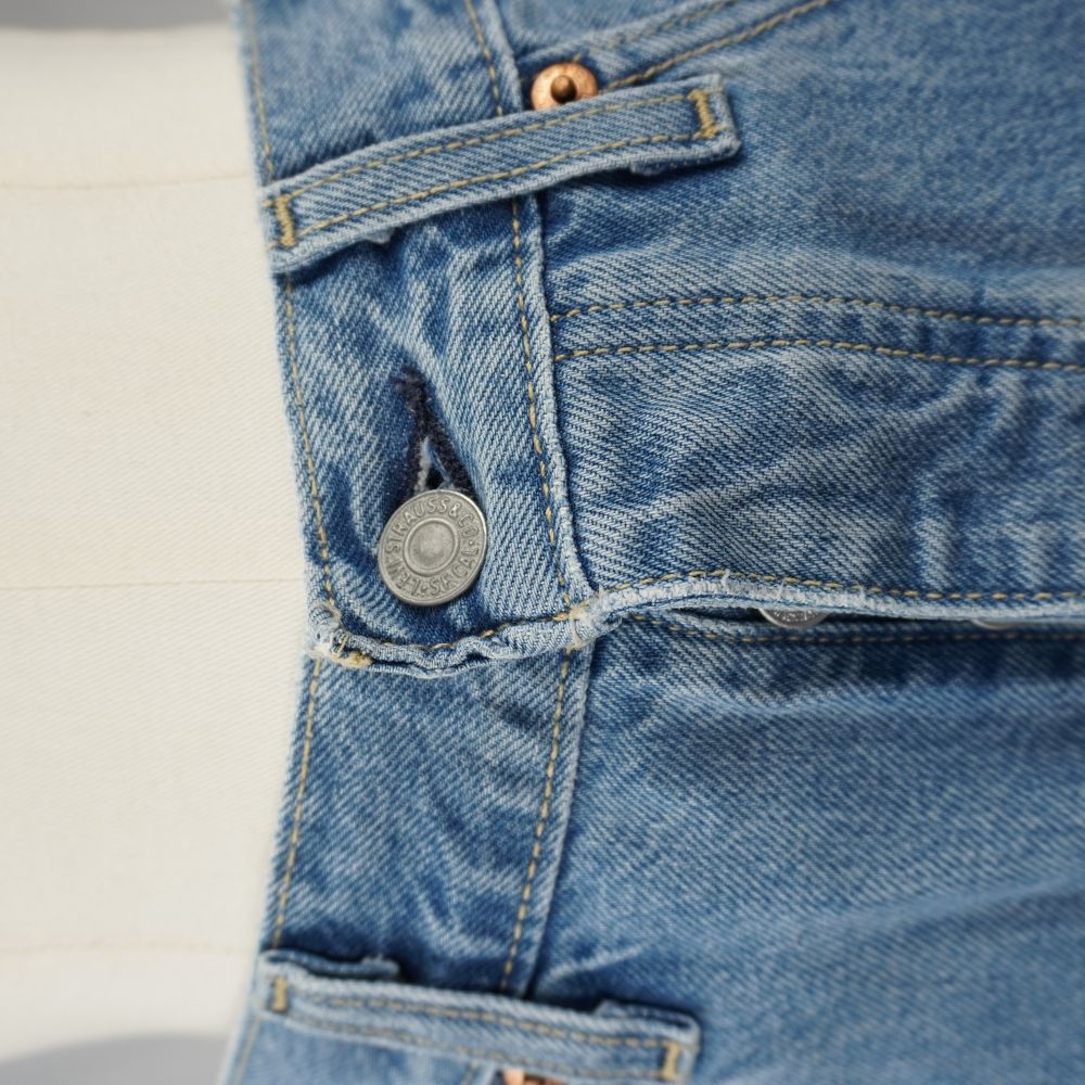 Dettaglio ravvicinato della chiusura in vita della gonna con bottone metallico a chiodo inciso Levi Strauss e patta tradizionale.