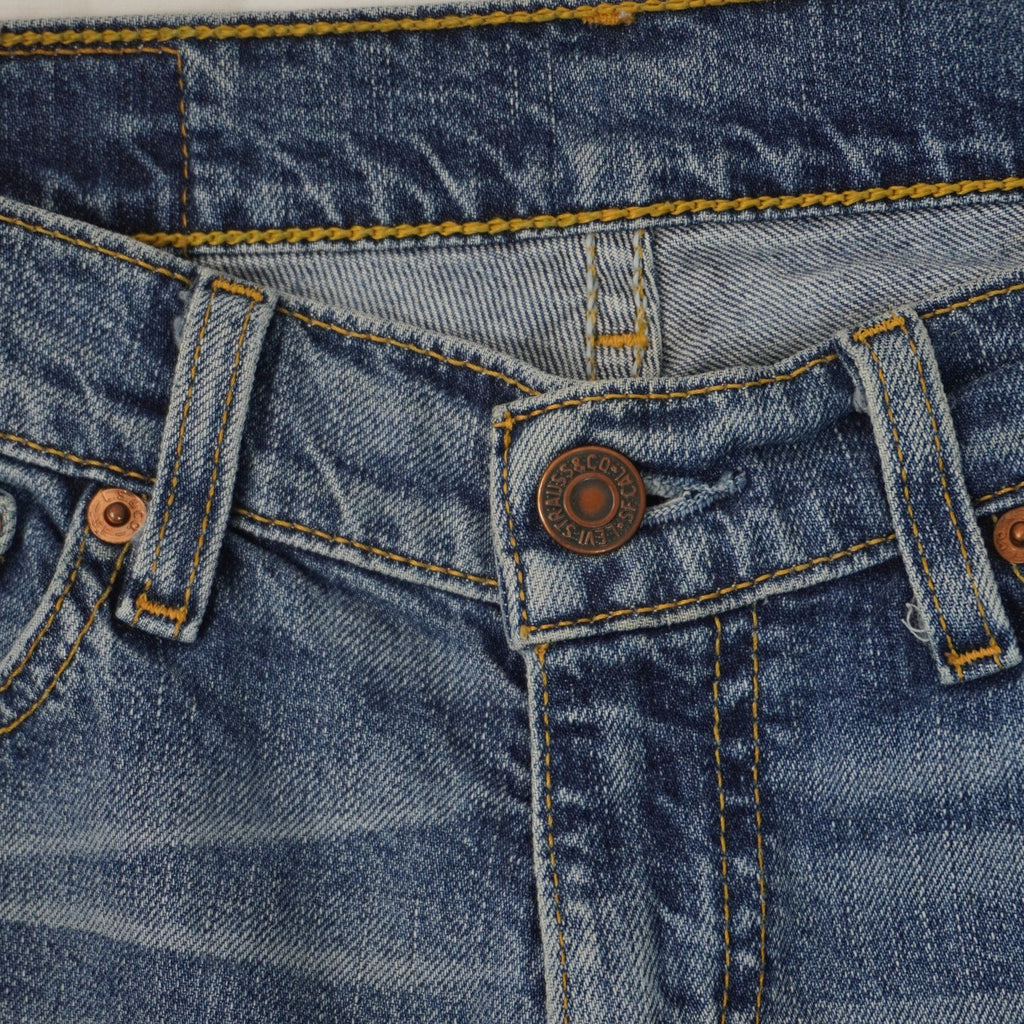  Primo piano della chiusura frontale dei jeans con bottone metallico inciso e finiture delle cuciture della patta.