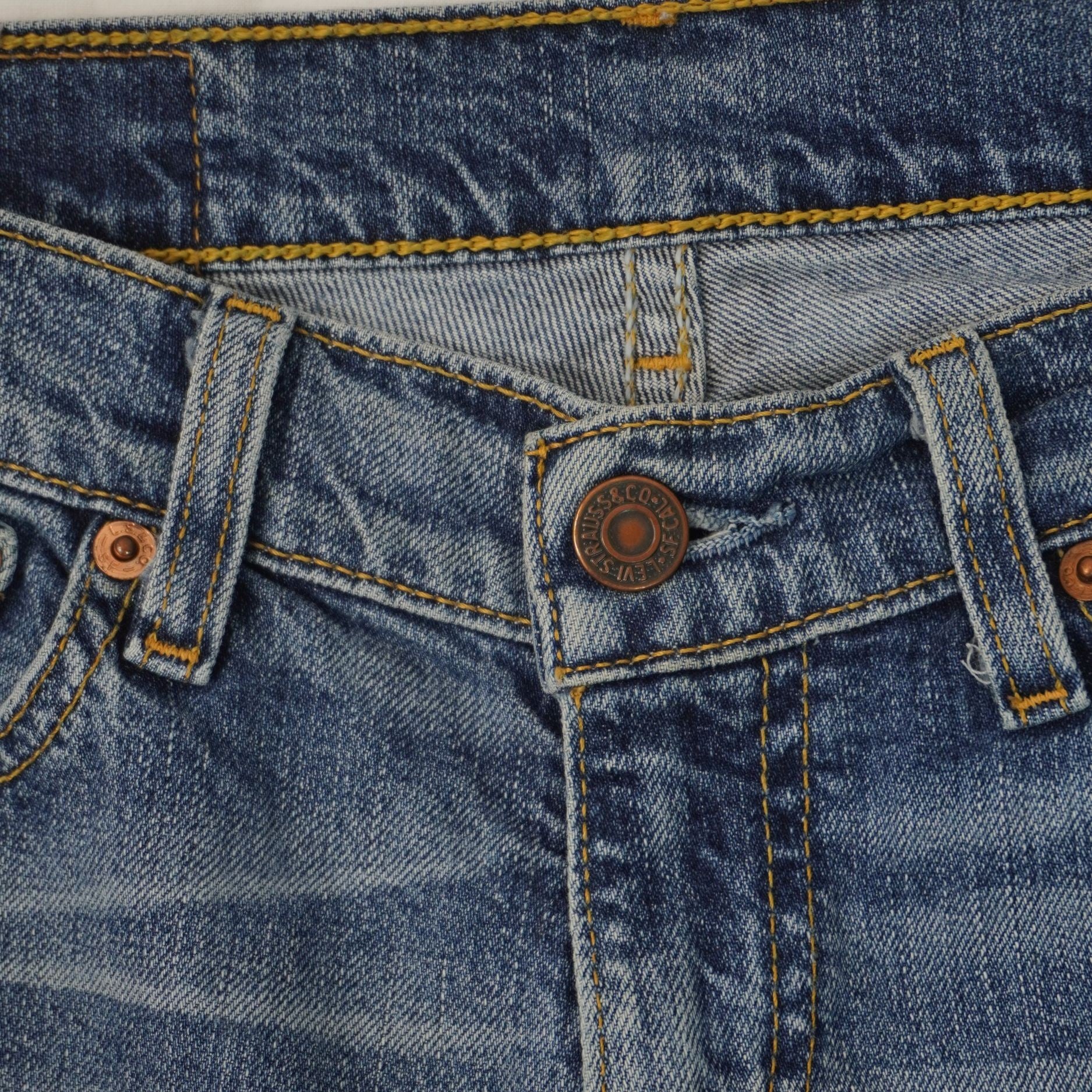  Primo piano della chiusura frontale dei jeans con bottone metallico inciso e finiture delle cuciture della patta.