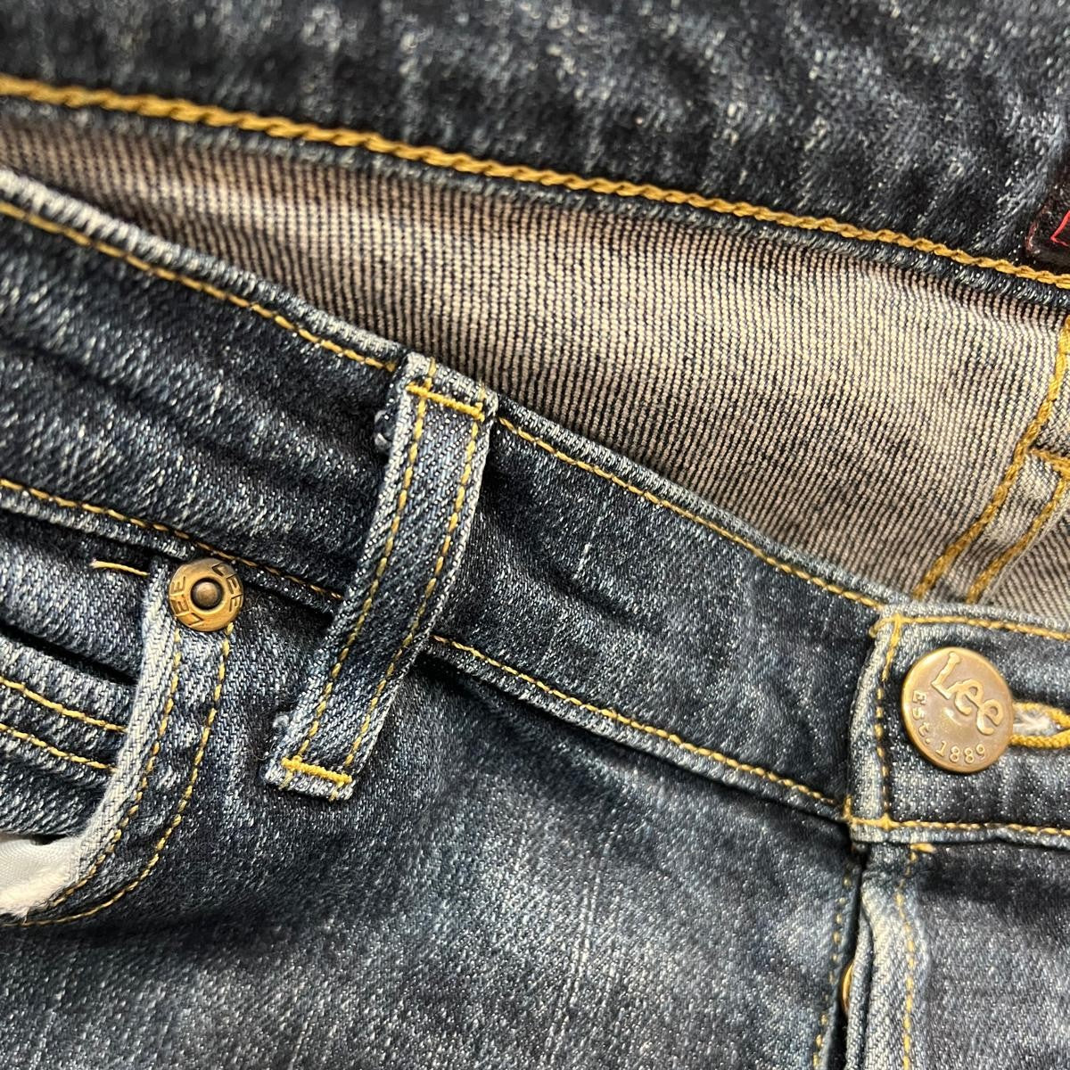 Primo piano della chiusura frontale dei jeans Lee con focus sui rivetti metallici di rinforzo e sulle cuciture delle tasche.