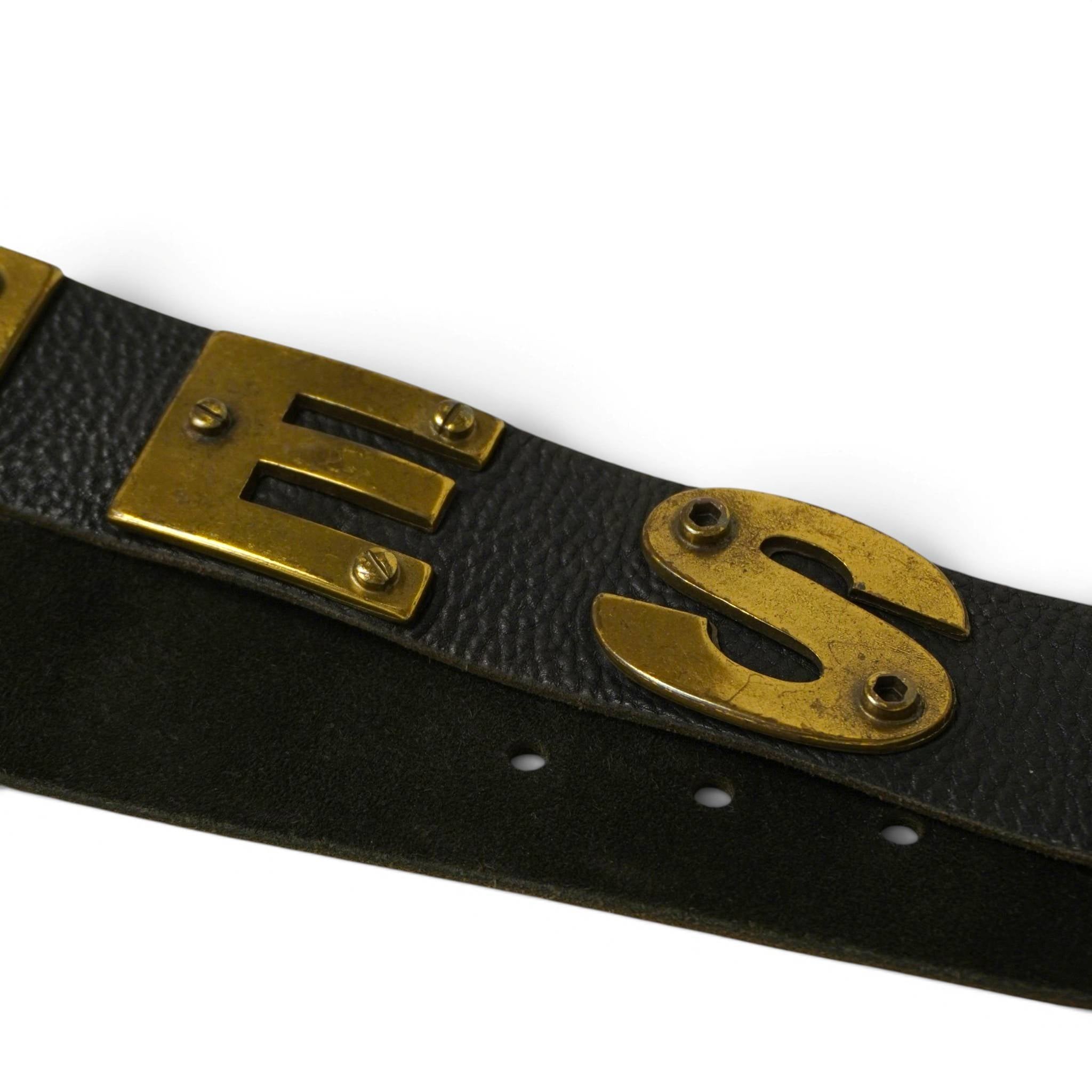 Primo piano delle lettere metalliche in ottone vintage E e S rivettate sul fusto in pelle nera.