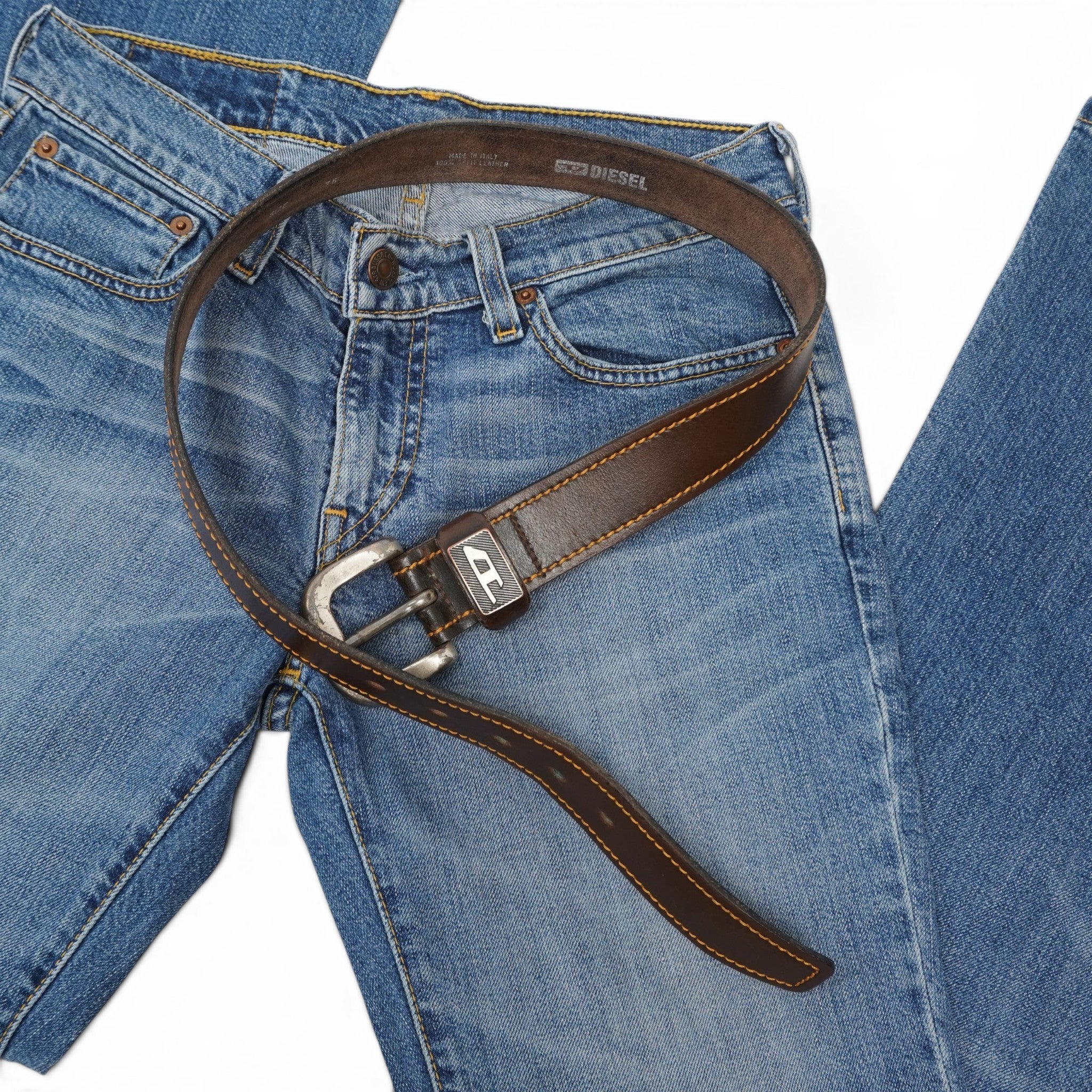 Vista dall'alto della cintura Diesel in pelle marrone posizionata sopra un paio di jeans in denim blu.