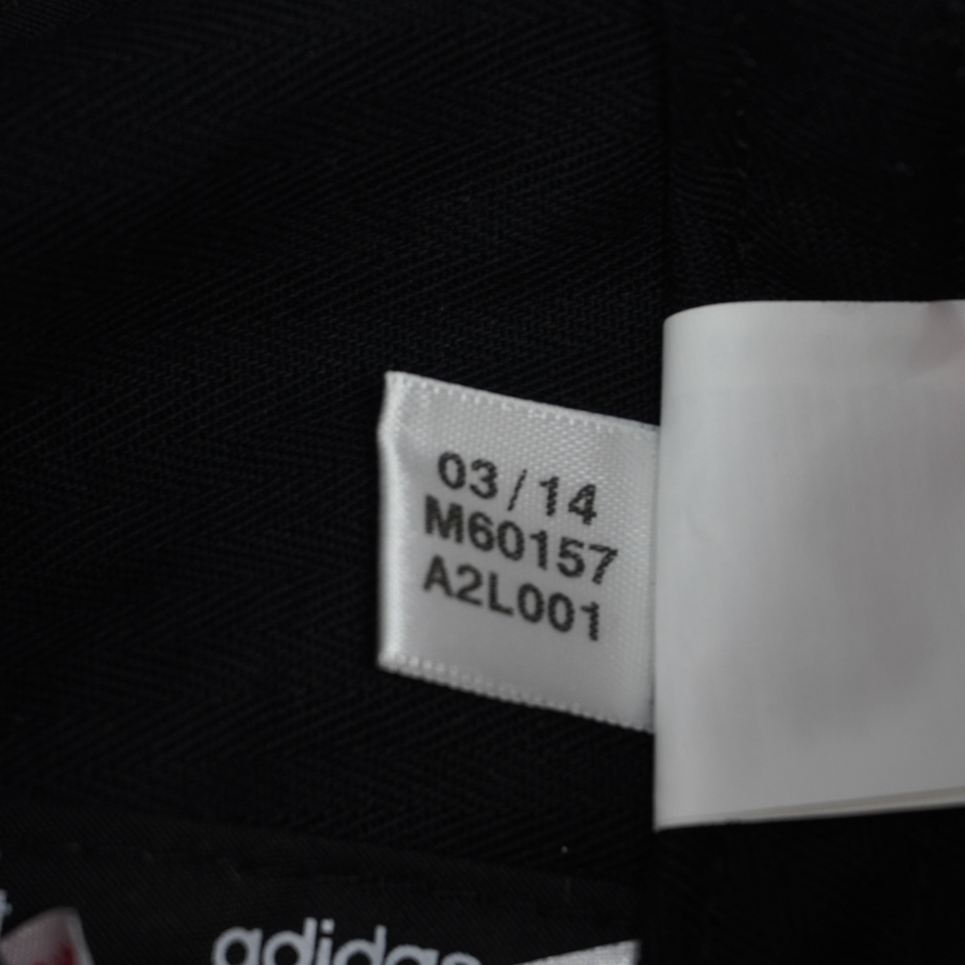 Macro del piccolo tag bianco Adidas con data di produzione 03/14 e codice articolo d'archivio M60157.