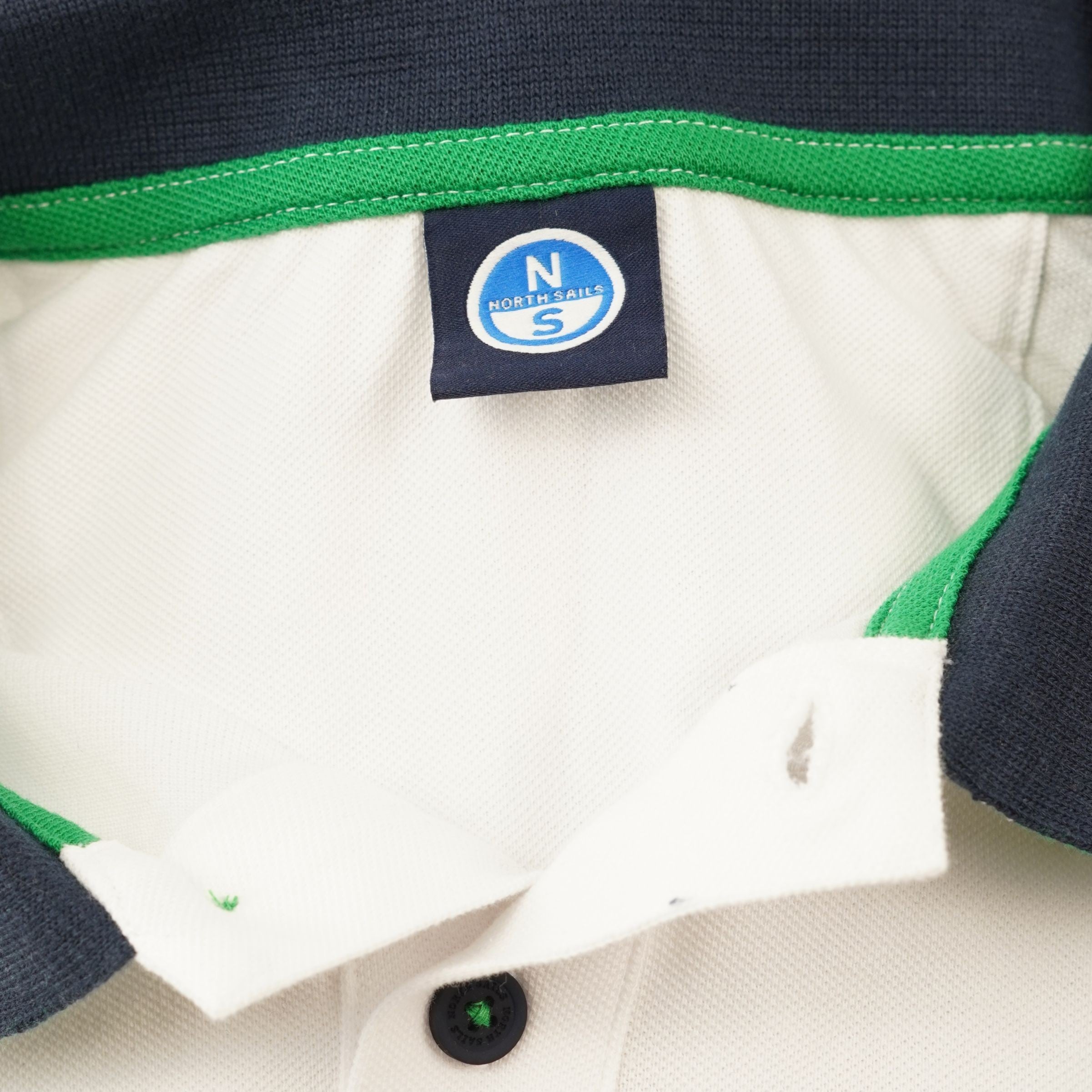  Primo piano del colletto interno della polo con fettuccia di rinforzo verde accesa ed etichetta blu quadrata North Sails.