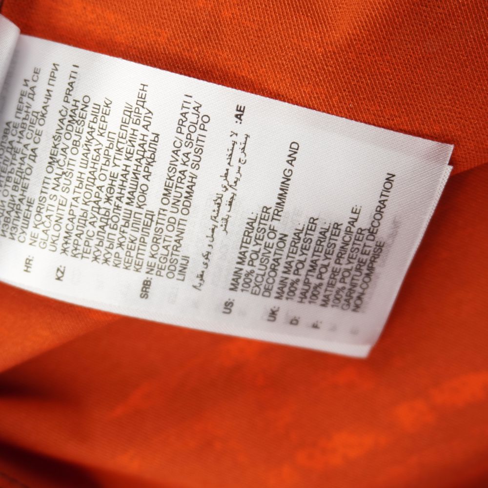 Vista posteriore dell'etichetta interna con l'elenco multilingua che certifica la composizione del materiale in 100% poliestere.
